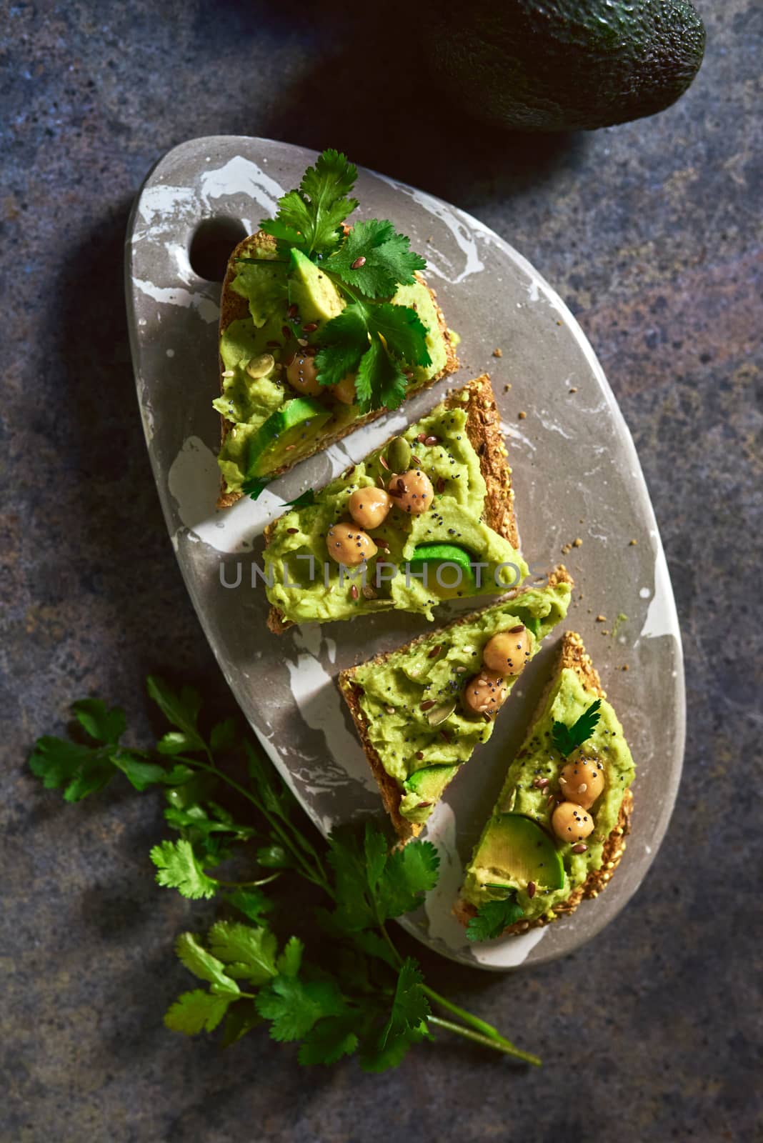 Toast of avocado hummus, decorated with chickpeas on stone table