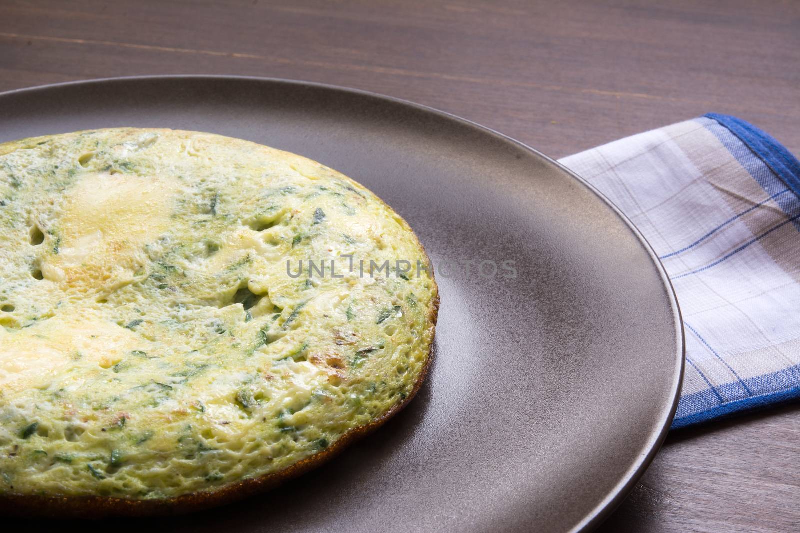 Omelet with spinach and zucchini with melted cheese on brown plate. wood table