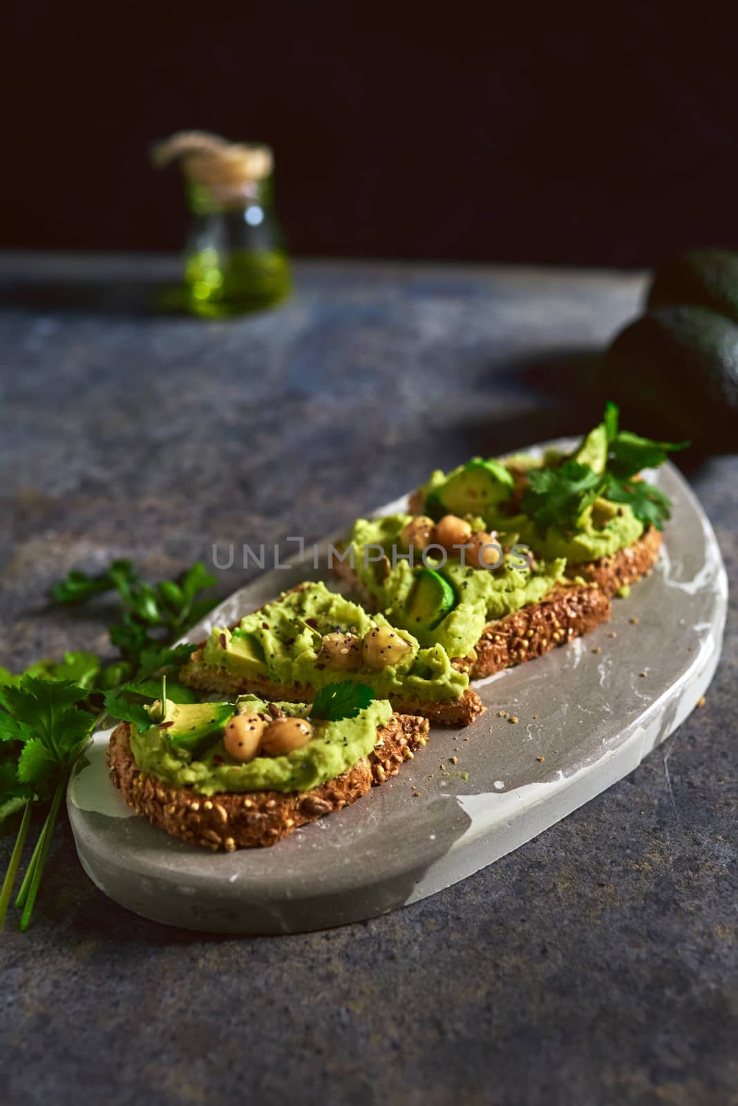 Toast of avocado hummus, decorated with chickpeas on stone table