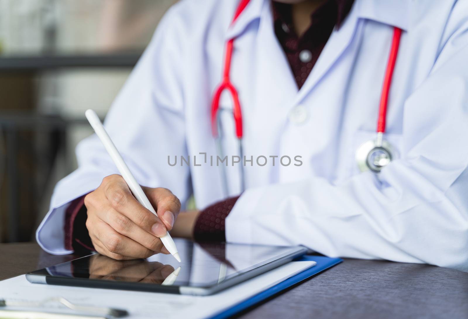 Close up shot hand of Doctors with stethoscope are using tablets to write treatment reports or view patient information. New normal of medical use remote technology for follow up and consult patients
