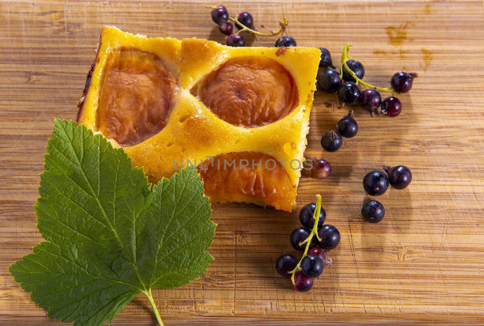 Cake with apricot and blackcurrant decorated with currant leaves on a wooden board