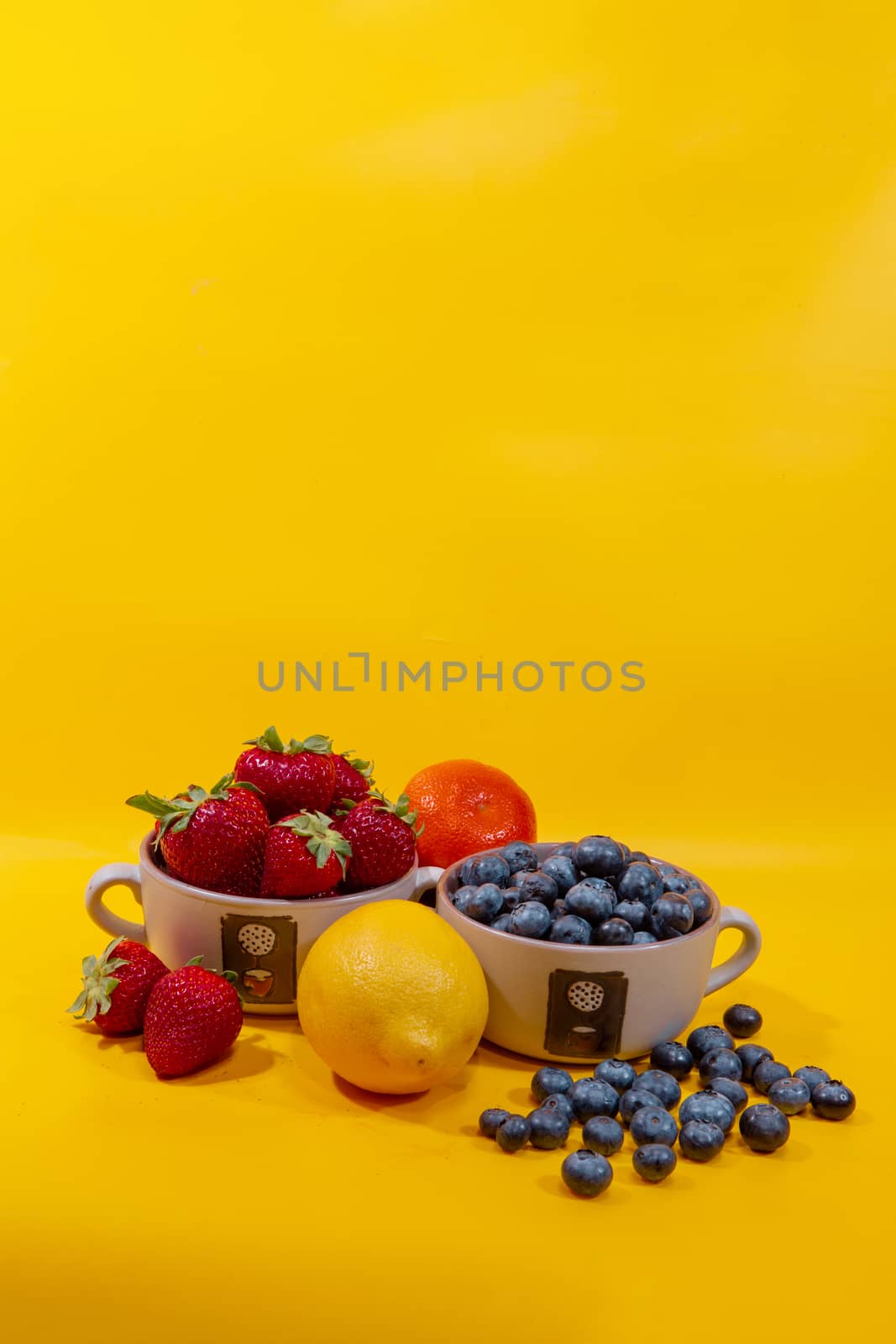 Blueberries and strawberries in ceramic cups against a yellow ba by ben44
