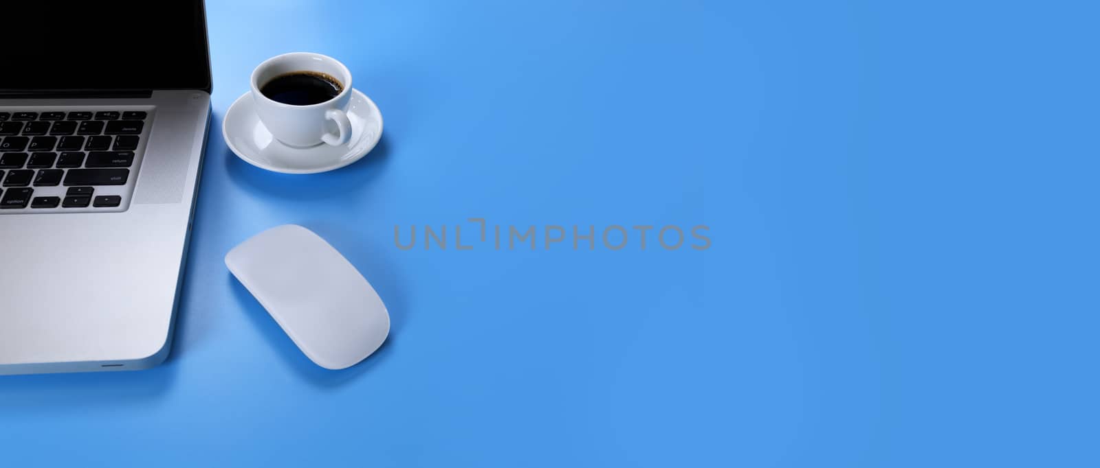 Laptop, mouse coffee on blue background. Laptop, mobile phone, black coffee isolated on blue background with copy space banner. Business concept.