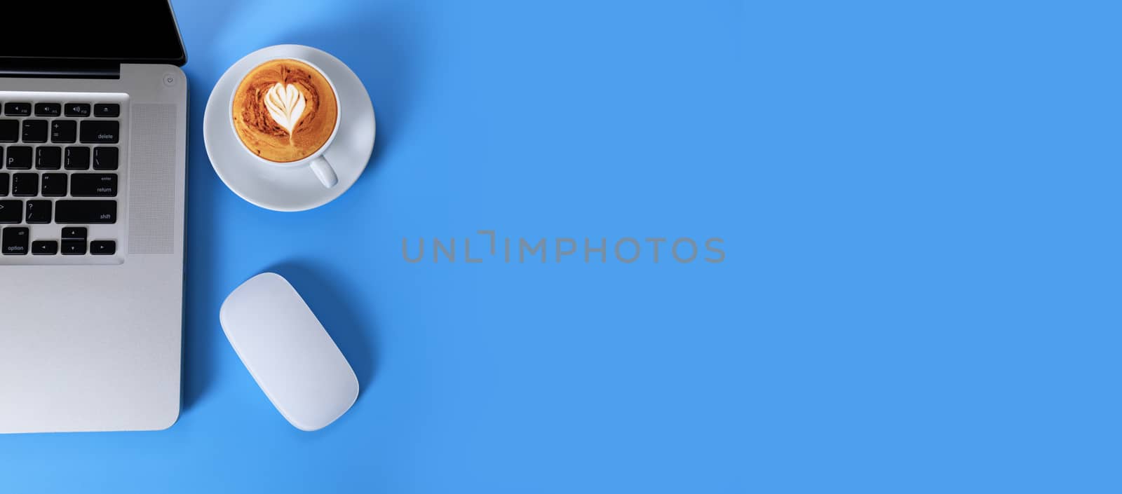 Top view Laptop, smartphone, coffee on blue background. Laptop, mobile phone, cappuccino coffee with heart shape isolated on blue background with copy space banner. Business concept.