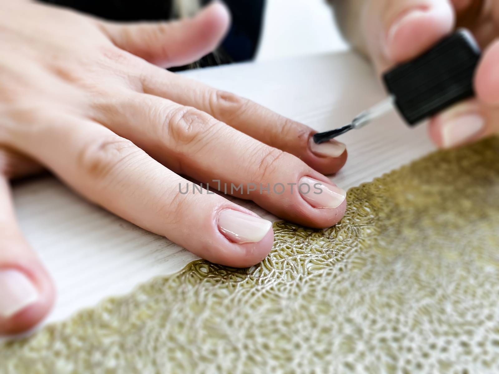 Hands of a female applying transparent nail polish on the nails with a black brush by rarrarorro