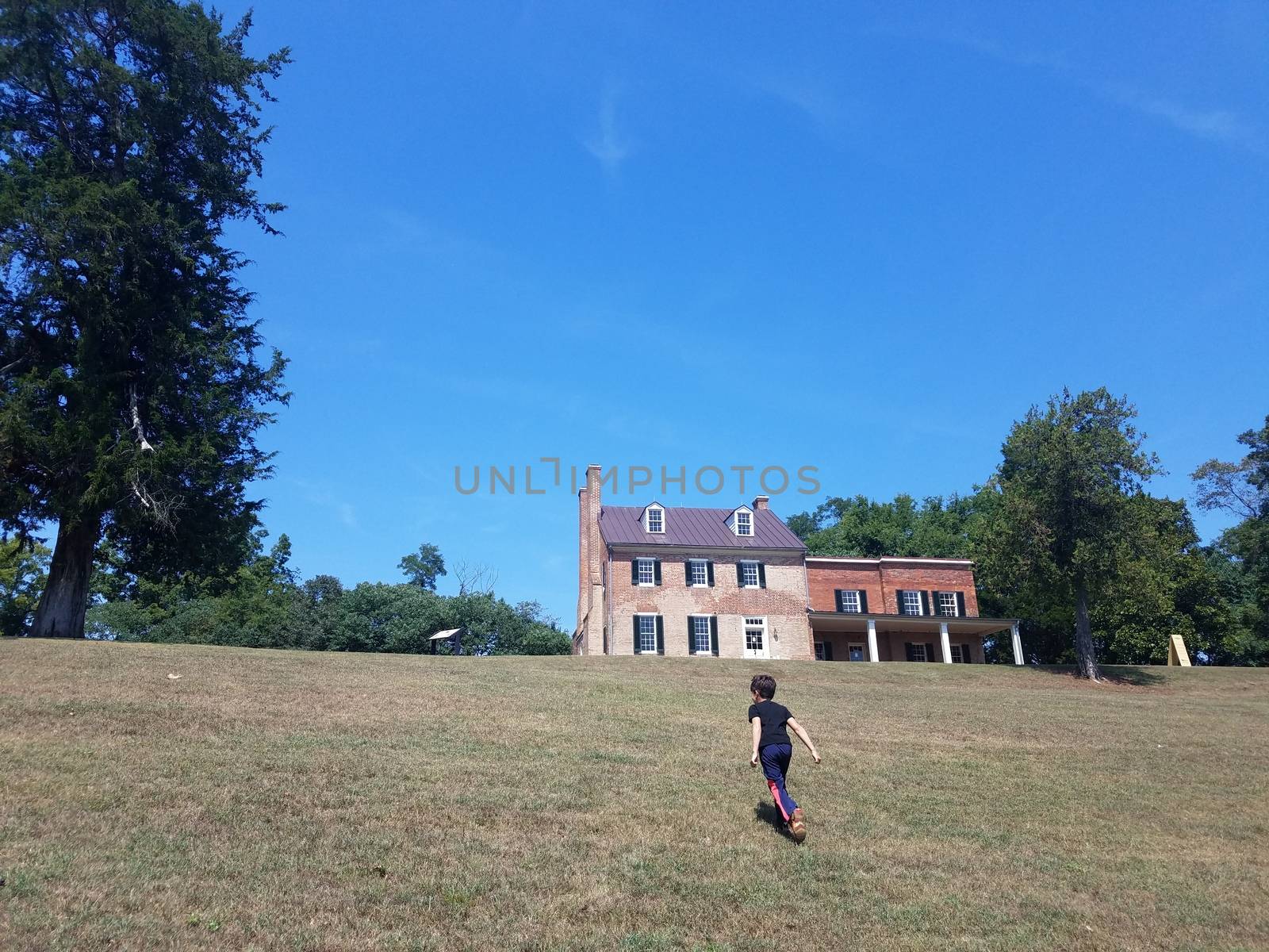 boy child running up hill or grass with building