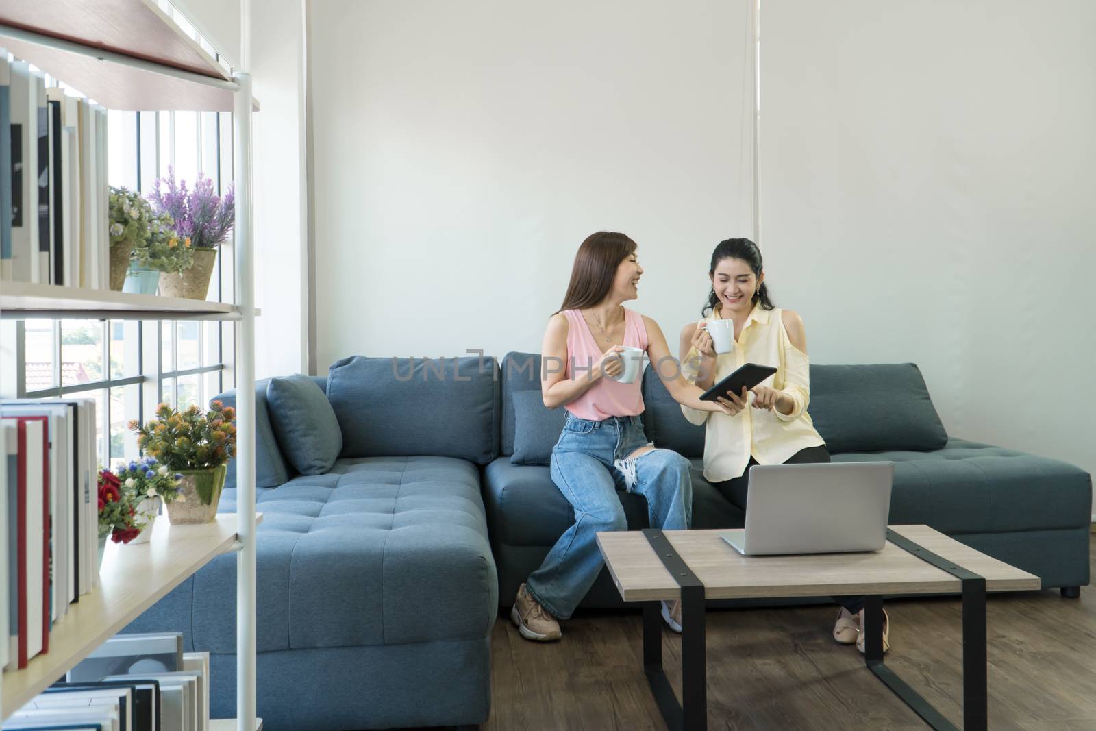 Two attractive Asian women are talking at home happily. Freelance women share casual wear, meetings, and computer technology together. learning use the internet  chatting with people on social media