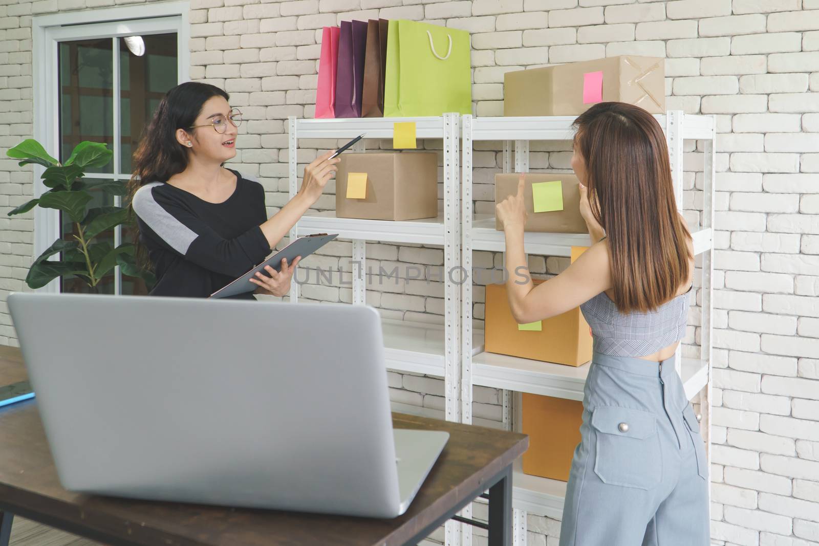 Merchant Two attractive young Asian women make living selling products online. They are checking the boxes to send customers. They use communication technology and the internet to market