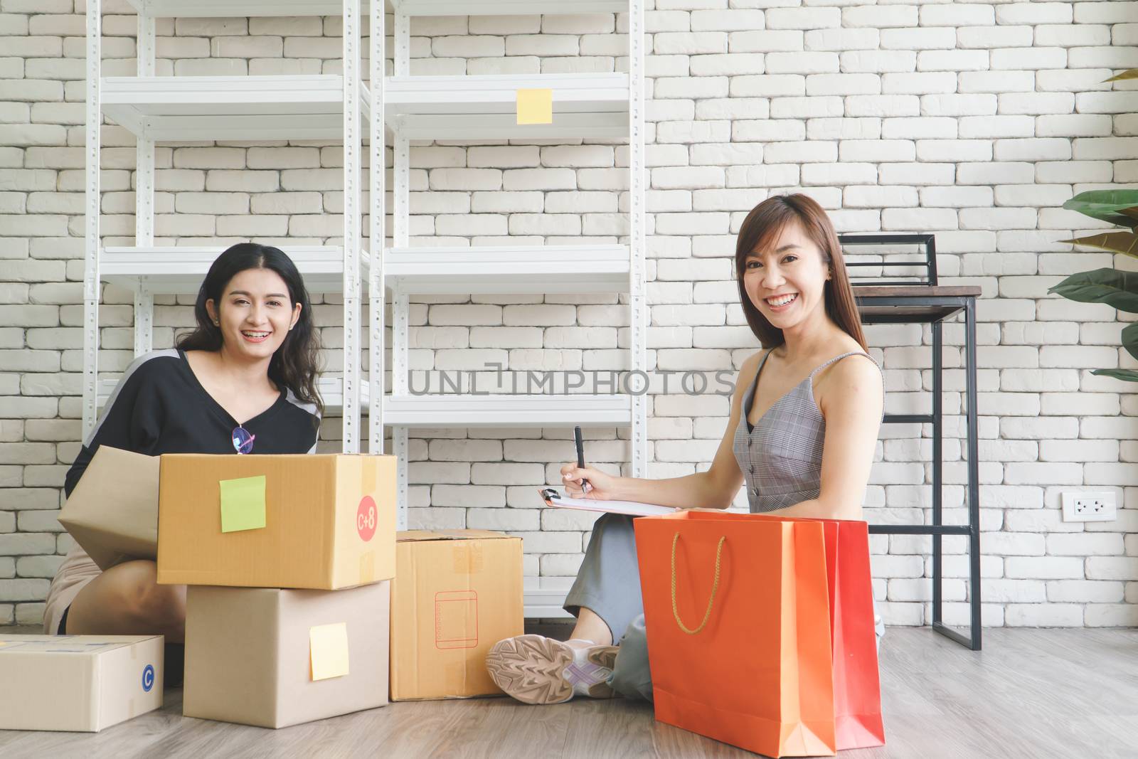 Merchant Two attractive young Asian women make living selling products online. They are checking the boxes to send customers. They use communication technology and the internet to market