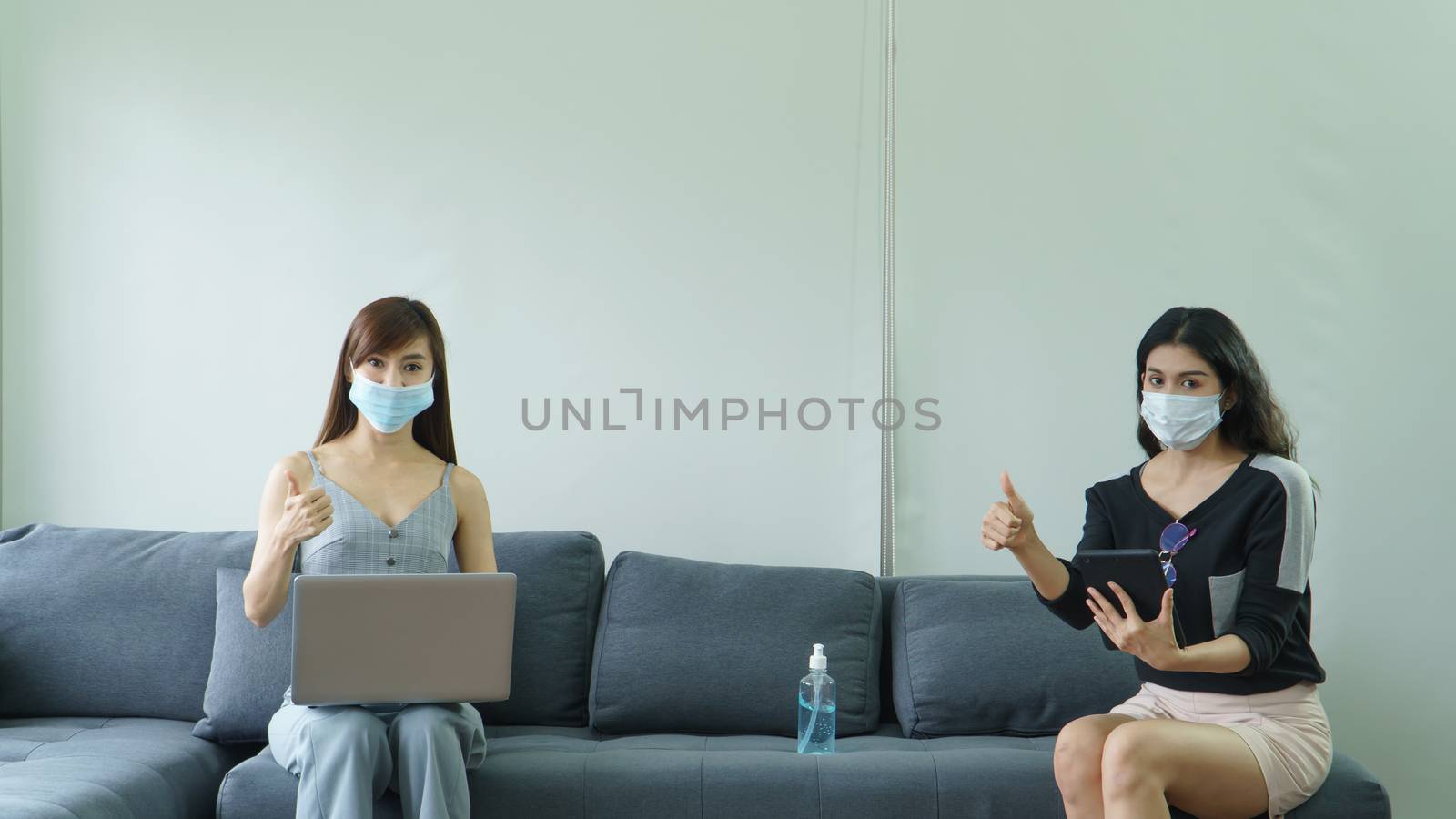 Coronavirus or COVID-19 is spreading. Two Asian women wearing medical masks Keep the distance Are using laptops and tablets at home .social distancing is a new normal life