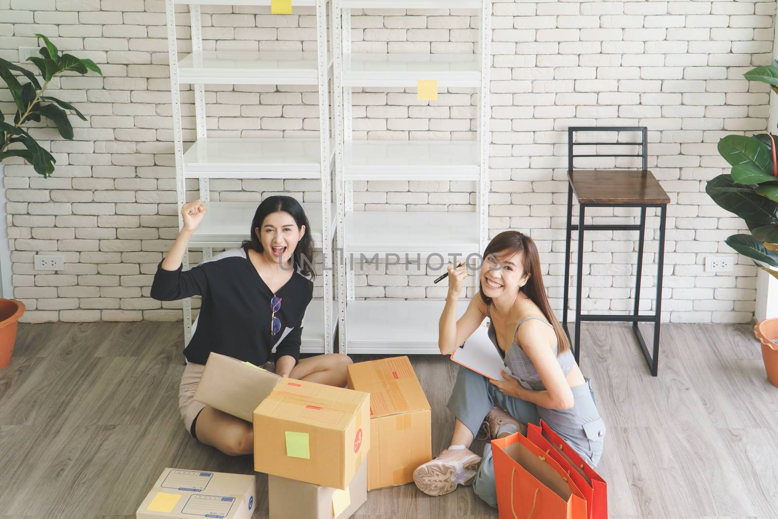 Merchant Two attractive young Asian women make living selling products online. They are checking the boxes to send customers. They use communication technology and the internet to market