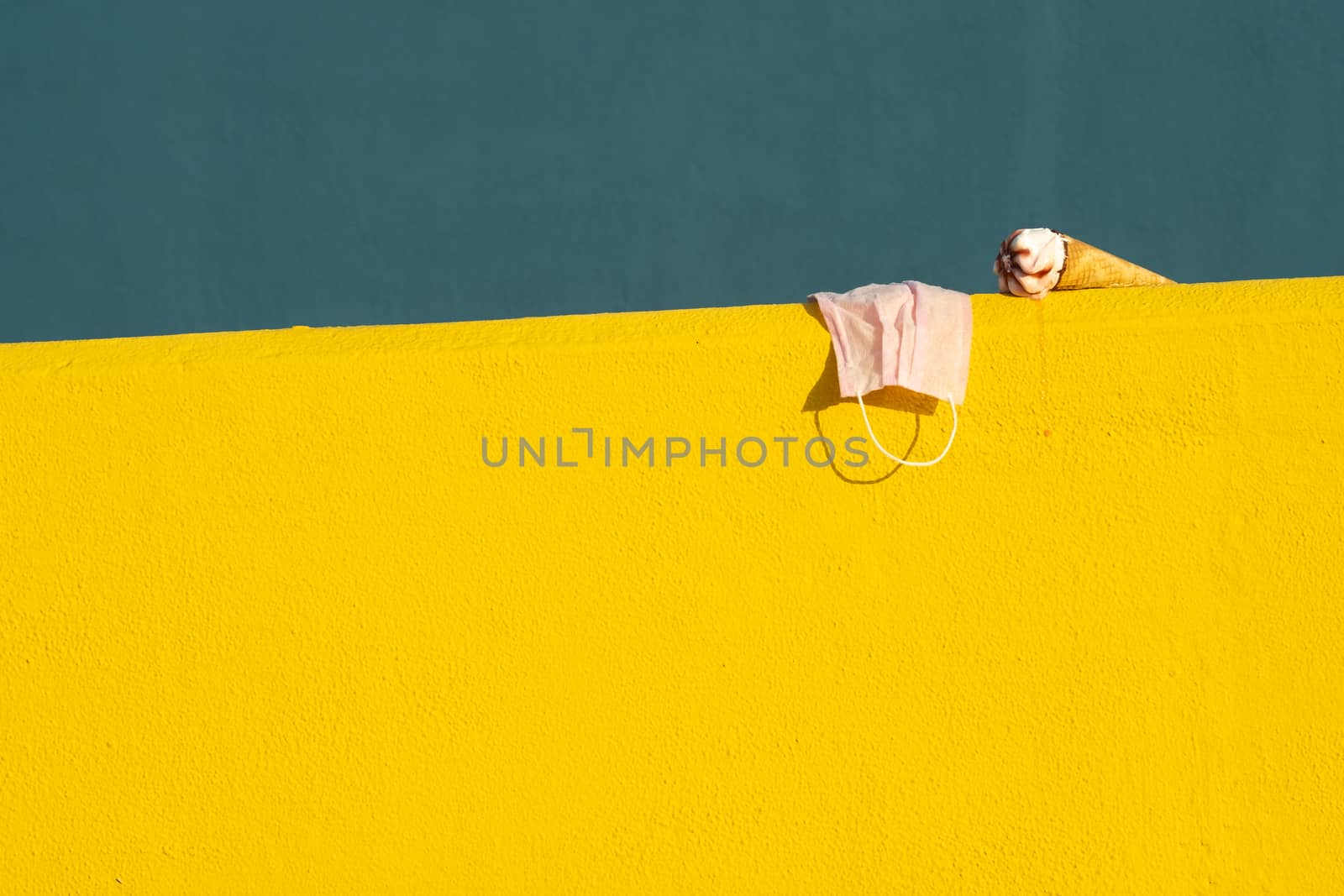 Covid-19 mask with ice cream with a cone melting in summer with the heat of the sun on a yellow and blue background. Holiday and coronavirus concept