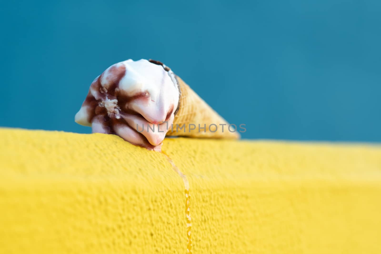 Ice cream with a cone melting in summer with the heat of the sun on a yellow and blue background. Vacation concept