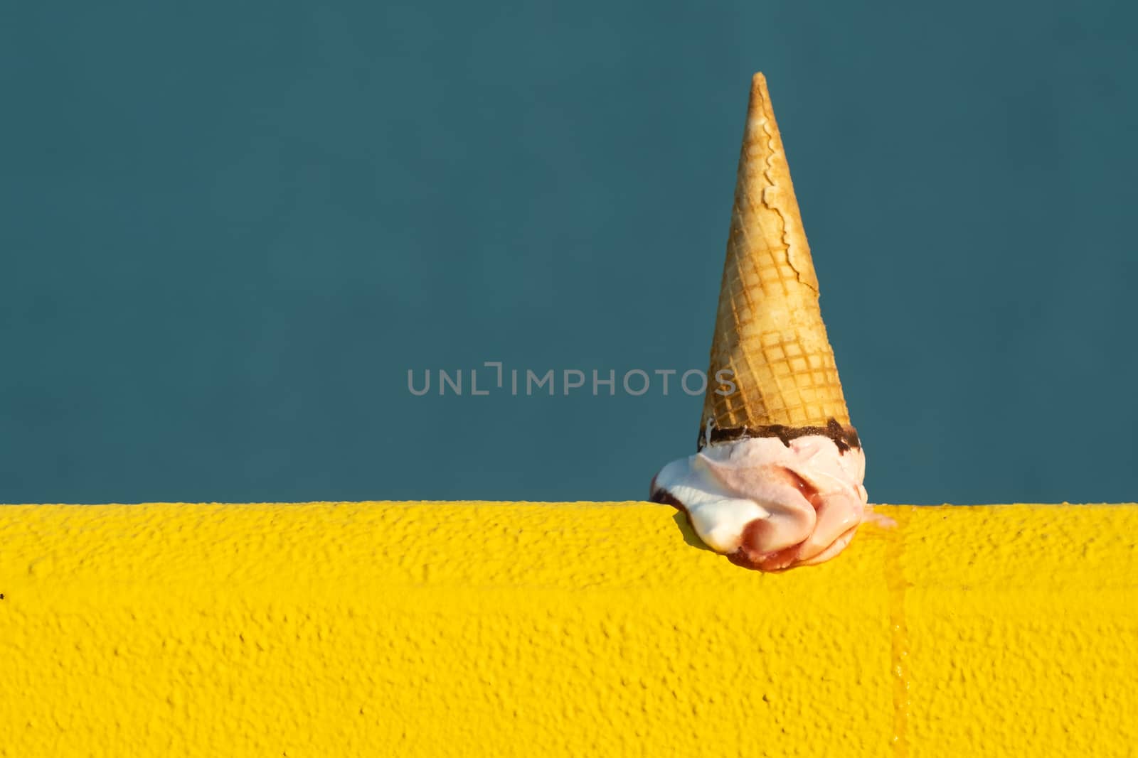 Ice cream with a cone melting in summer with the heat of the sun on a yellow and blue background. Vacation concept