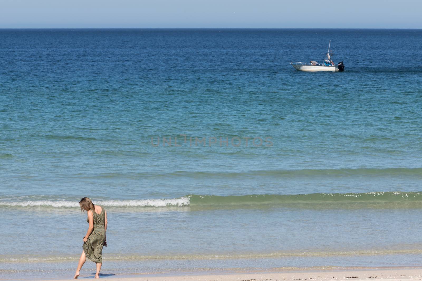 Middle-aged blonde woman in a green dress relaxes on the beach with a boat in the background