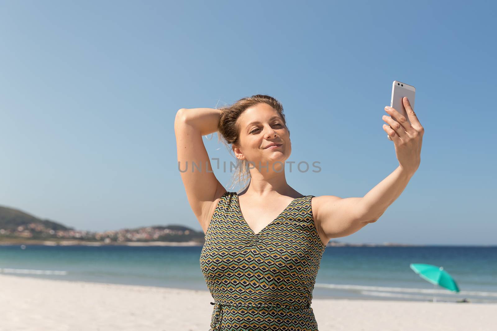 Middle-aged blonde woman in a green dress making a selfie on the beach with the sea in the background