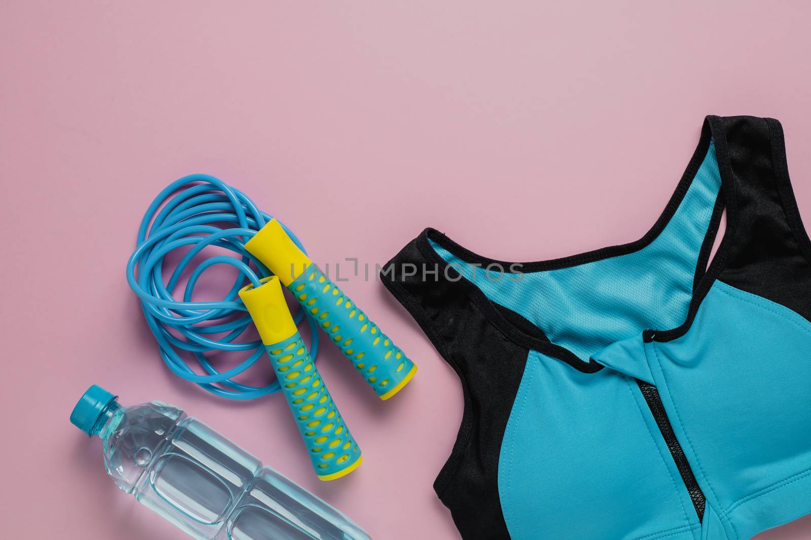 Sport bra for exercise, fresh drinking water and jump rope on pink background for sports and healthcare concept