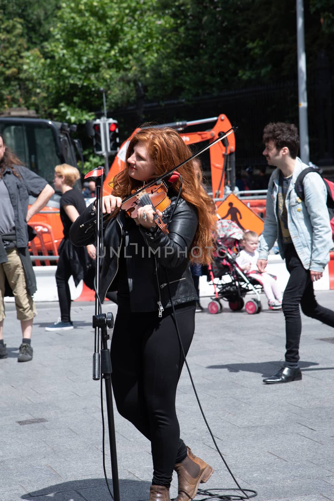 Dublin, Ireland--July 16, 2018. A musician playing the violin on the street with pedestrians in the background.