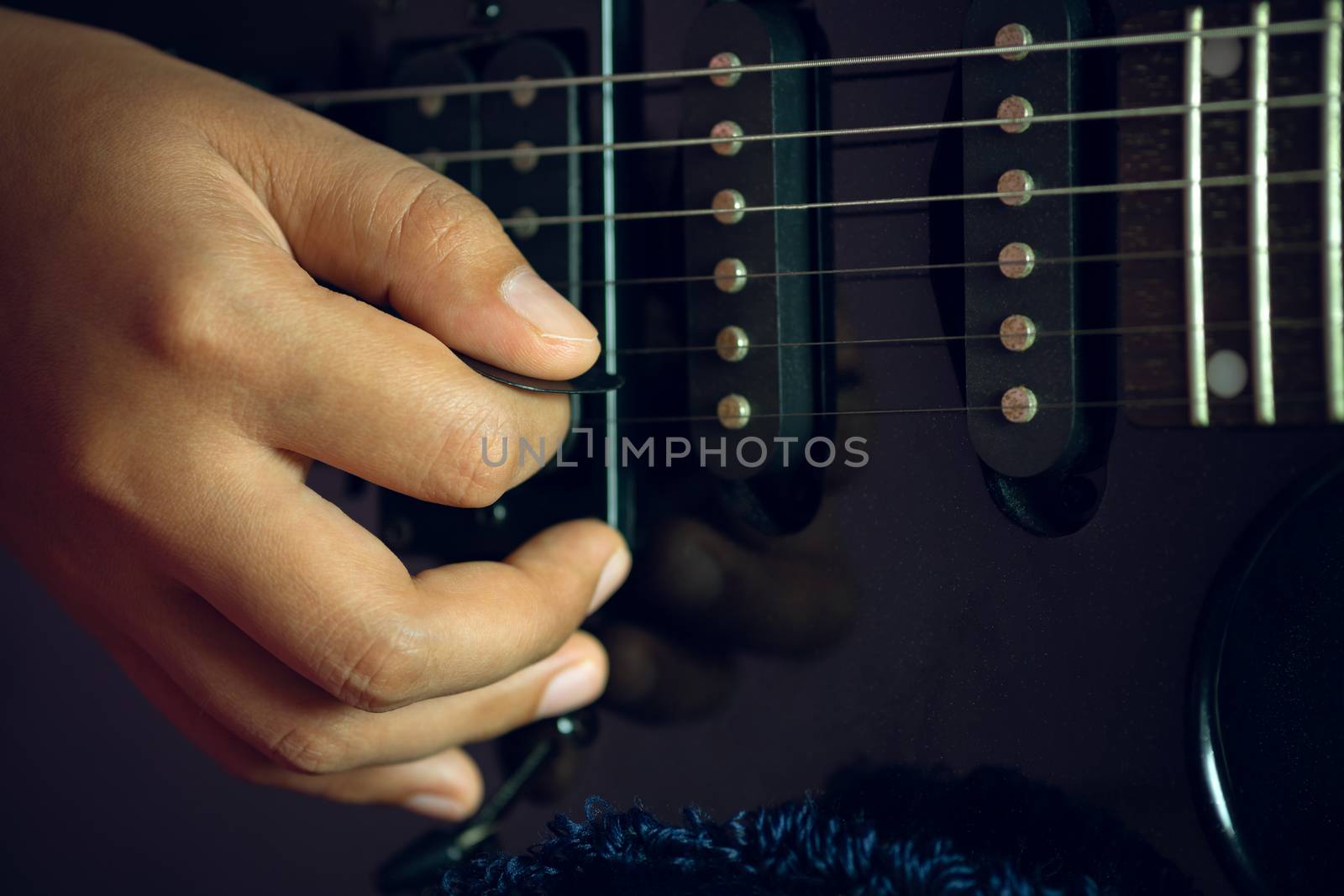 Guitarist is rehearsing playing black vintage electric guitars. Closeup  girl's hand is holding the pick and putting it on guitar string in dark studio. Concept of musical instruments and rock music.