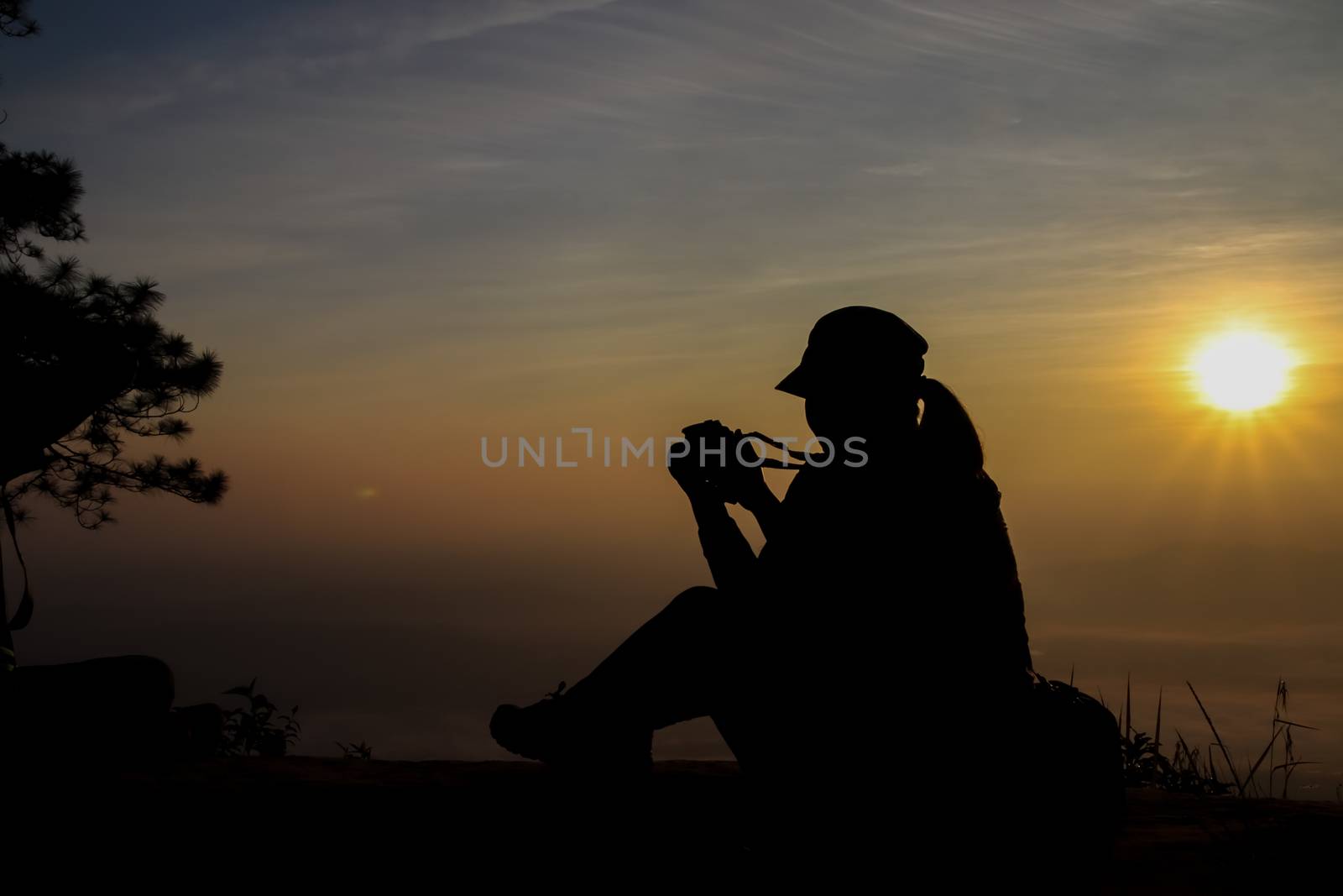 silhouette of a woman holding a camera taking pictures outside during sunrise or sunset by anotestocker