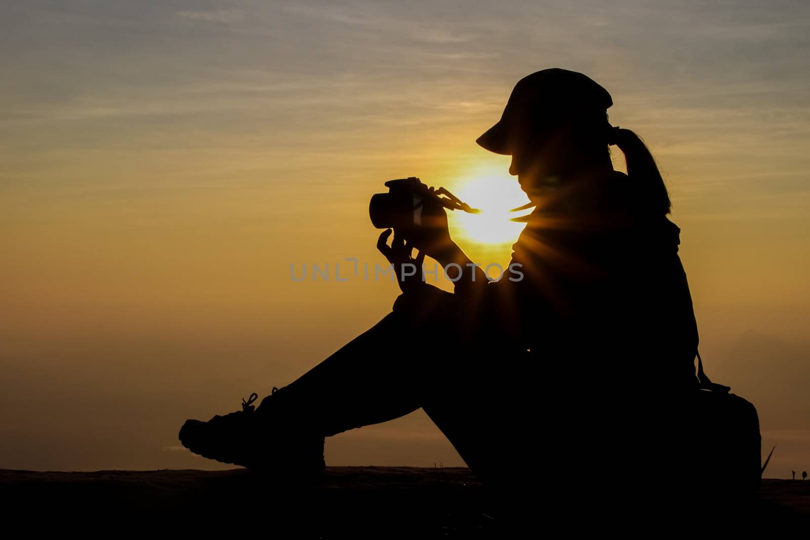 silhouette of a woman holding a camera taking pictures outside during sunrise or sunset