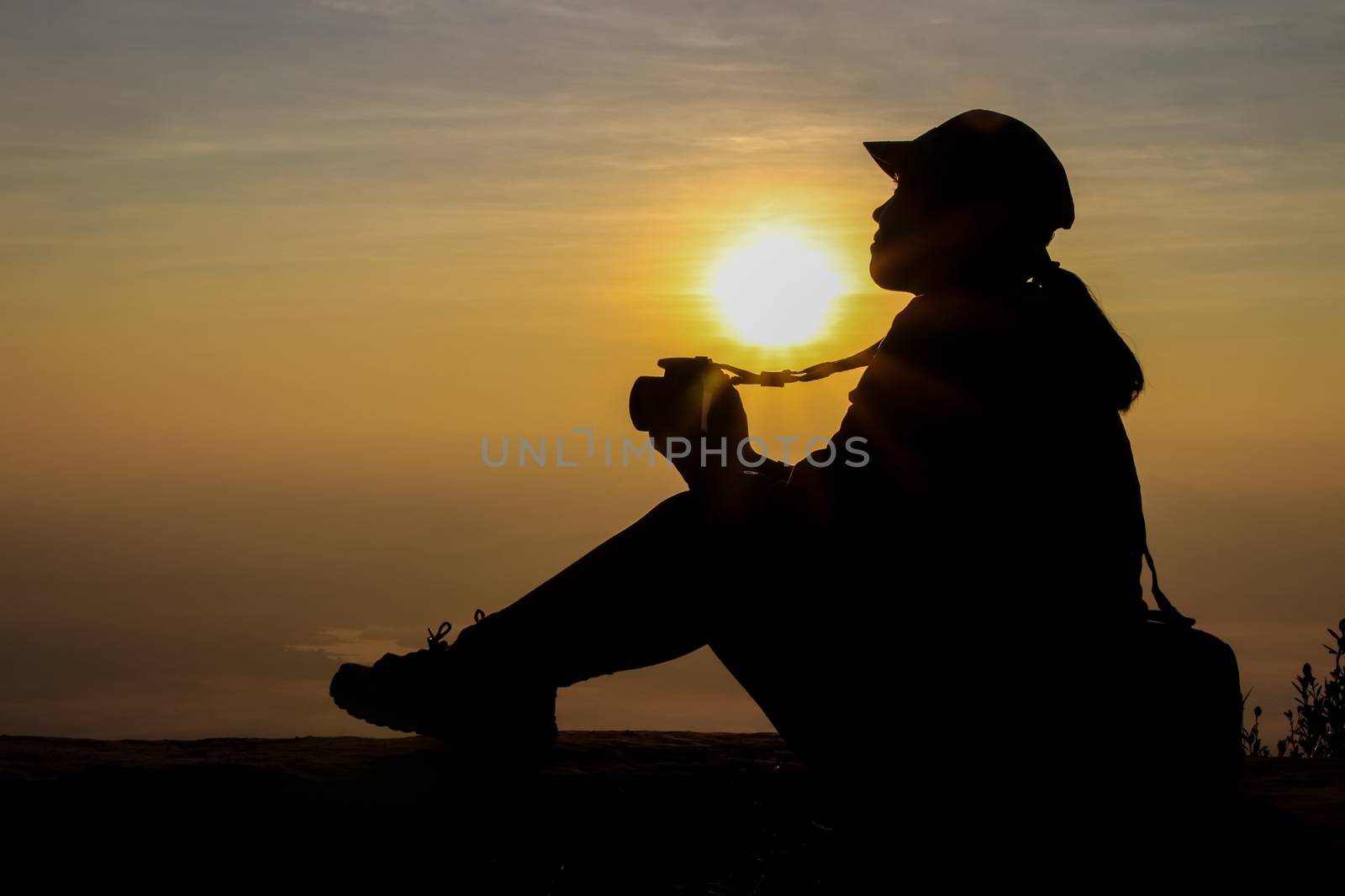 silhouette of a woman holding a camera taking pictures outside during sunrise or sunset