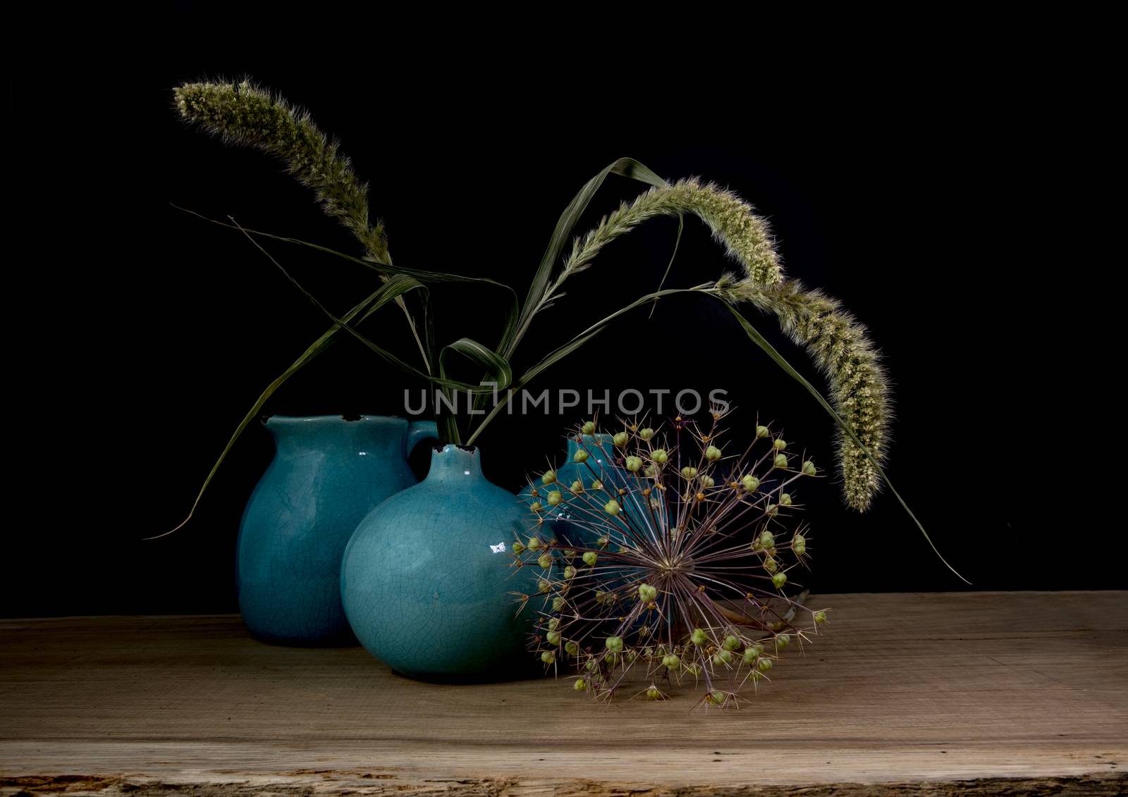 still life with three blue vases, ears of corn and a flower of an onion bulb on a dark background with light from the right side