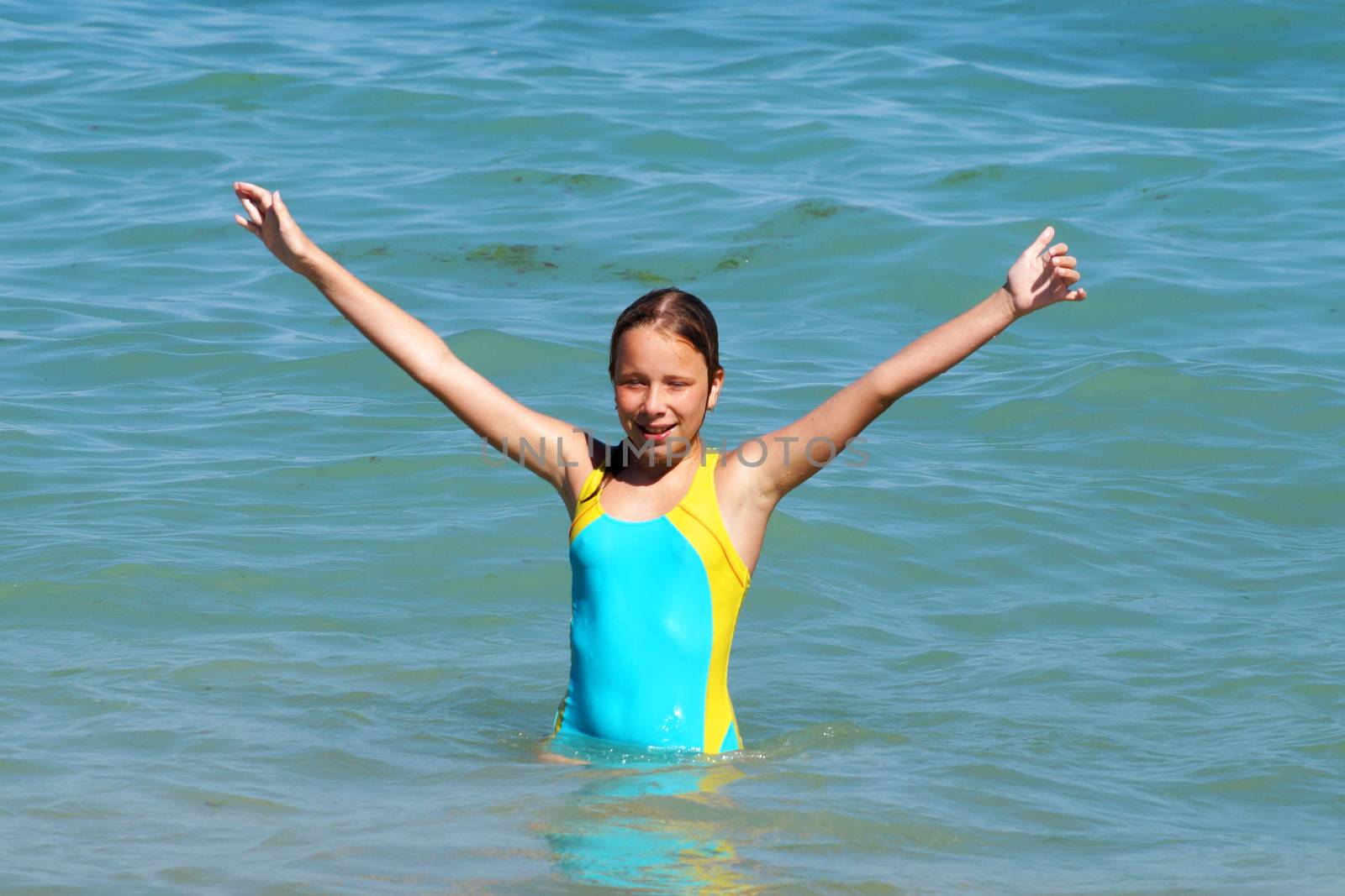 girl with hands up smiling at sea.
