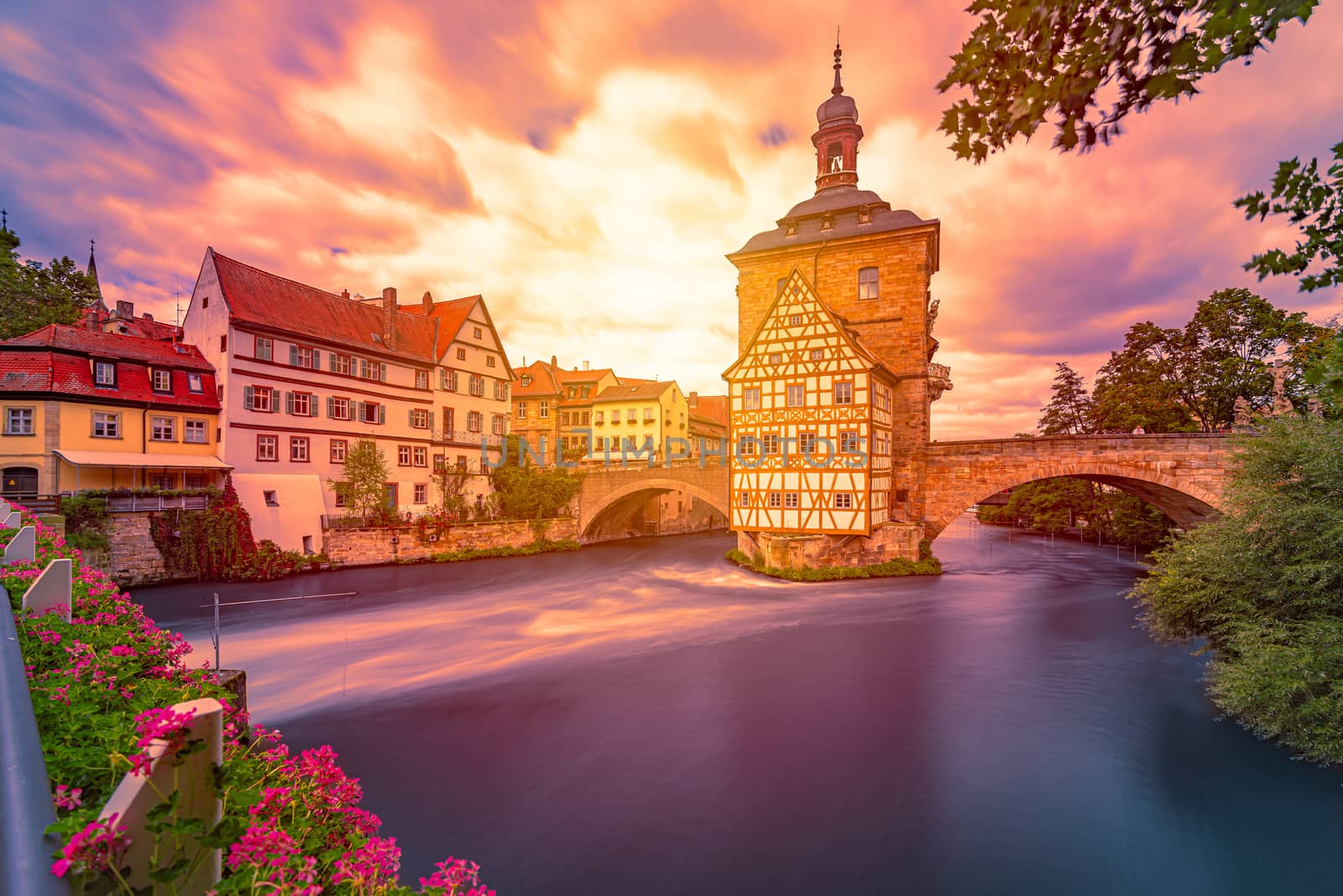 Bamberg city in Germany. Town hall building in background with blue cloudy sky.  Architecture and travel in Europe. Flowing river in foreground.