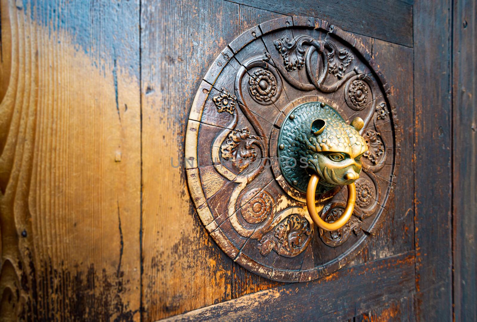 Detail of old wooden door with metal handle on board with carved pattern. Dark brown solid front door in vintage and antique style. Exterior and facade.