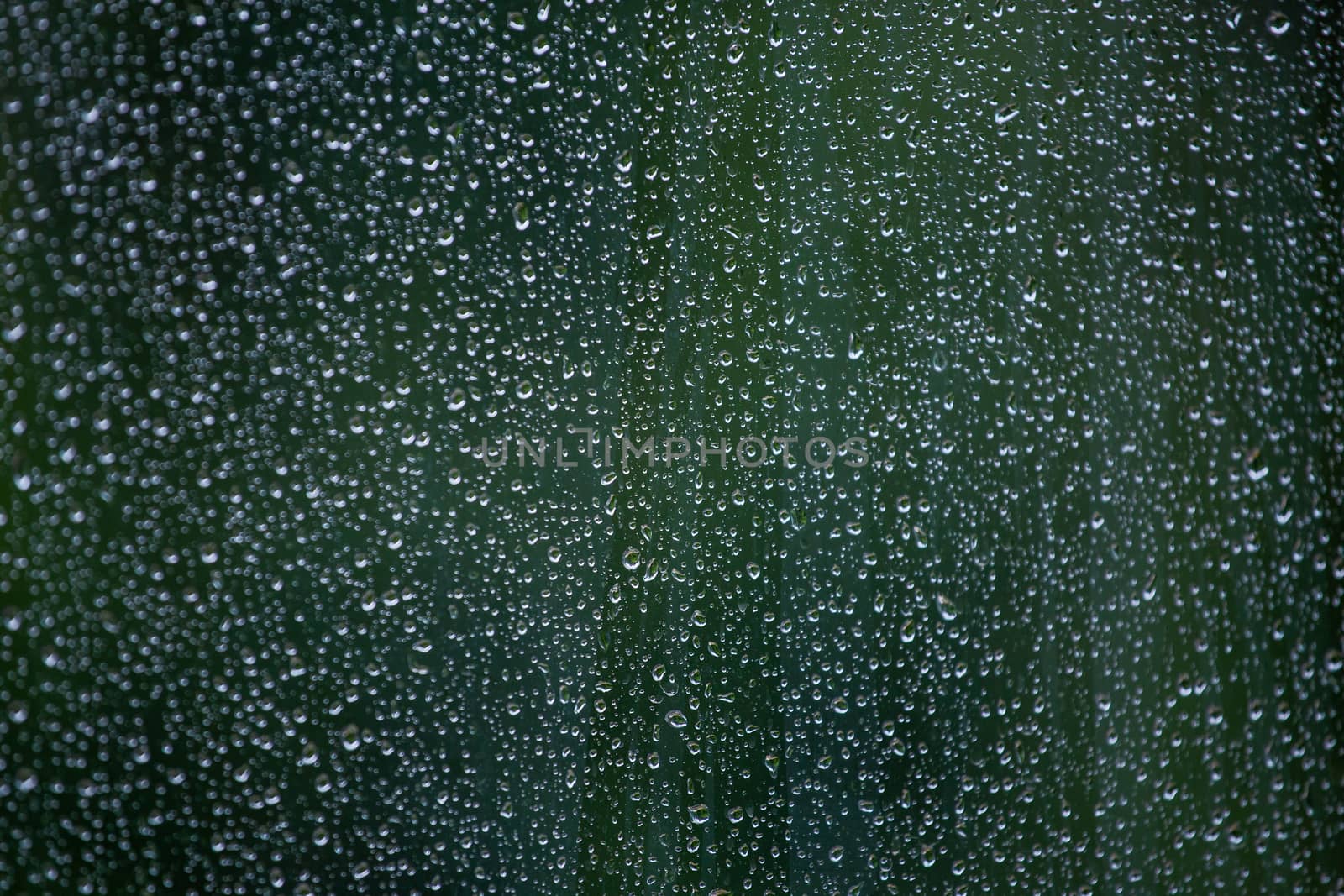 Abstract background of wet window glass with rain water drops. Summer cold green blurred backdrop and selective focus.