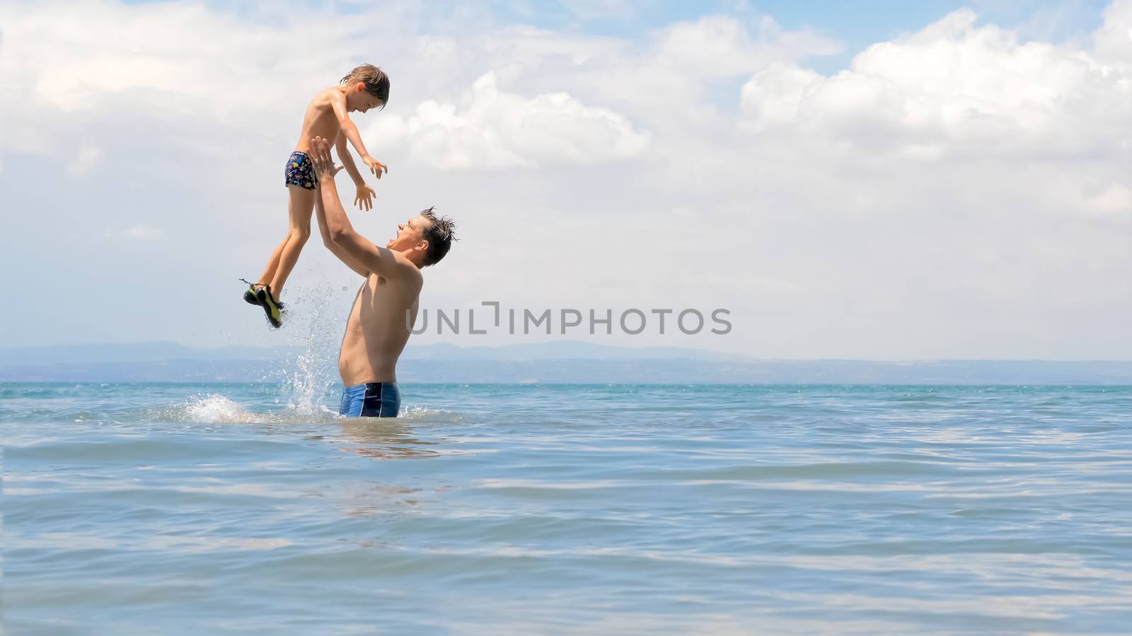 Happy european family playing at the sea. Dad and little son play and enjoy the sea water on the shore of lake, sea or ocean. Family vacation. Family tours, trips. Father playing with son at sea shore