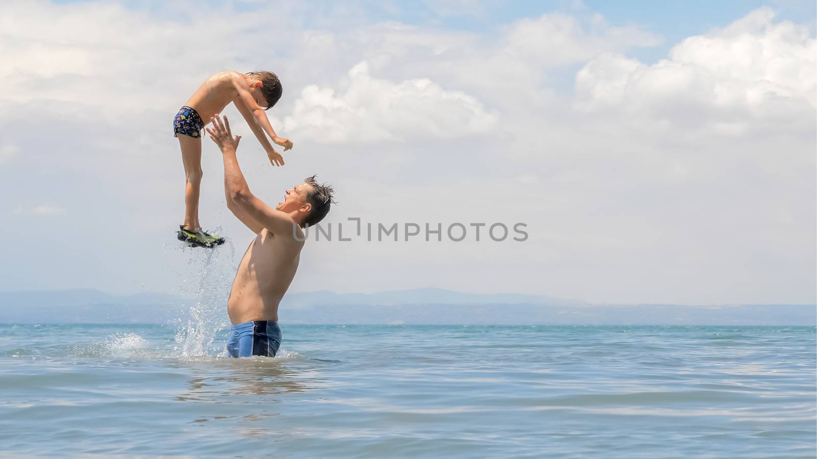 Happy european family playing at the sea. Dad and little son play and enjoy the sea water on the shore of lake, sea or ocean. Family vacation. Family tours, trips. Father playing with son at sea shore