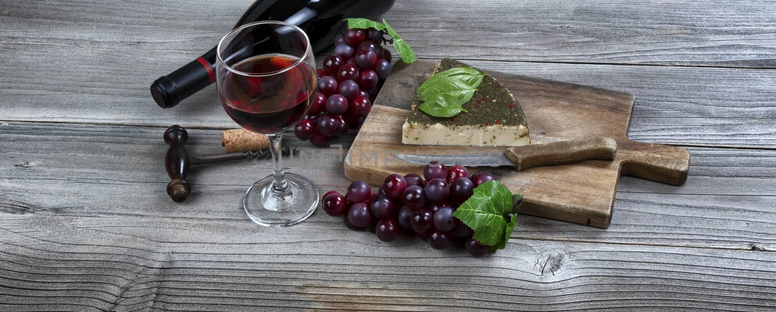 Glass of red wine with cheese wedge plus basil leaves and grapes by tab1962