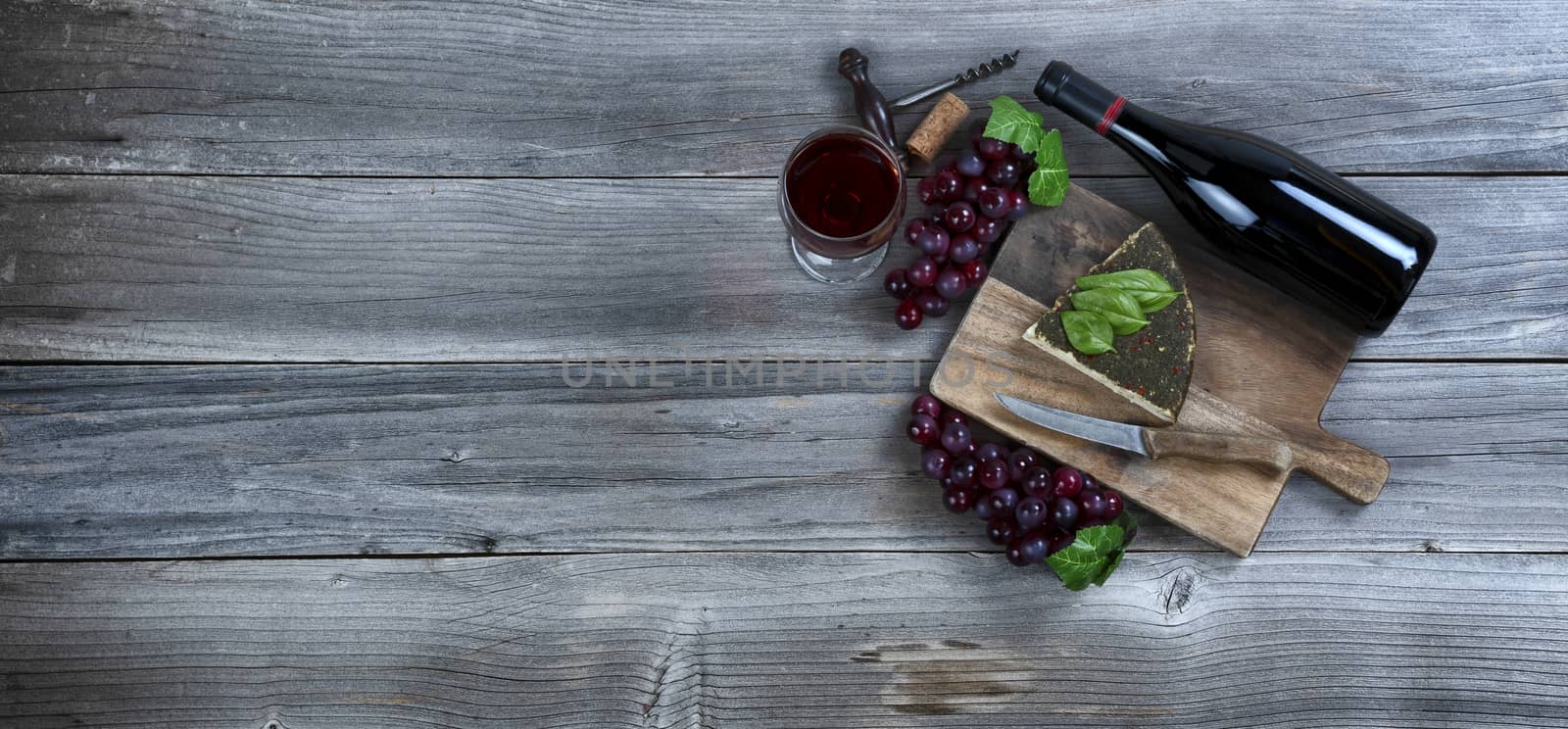 Red wine with fresh cheese wedge plus basil leaves and grapes on rustic wood with copy space available 