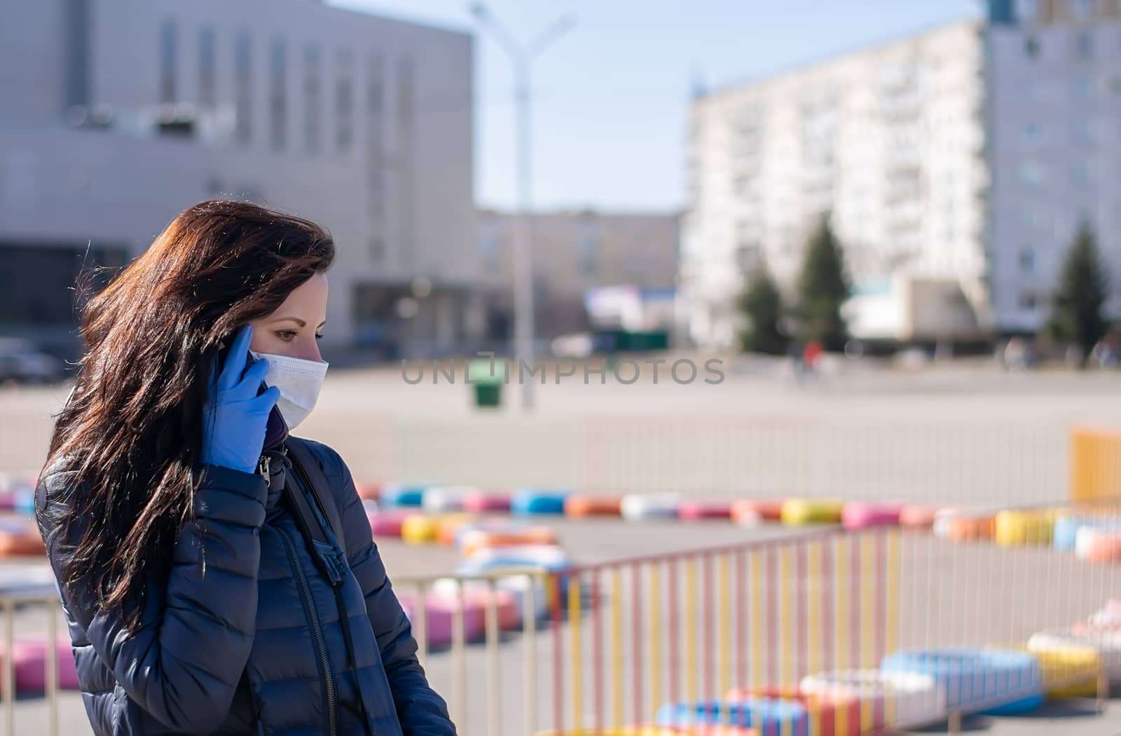 a girl in an antibacterial mask and rubber gloves on a city street with a sad face talking on the phone