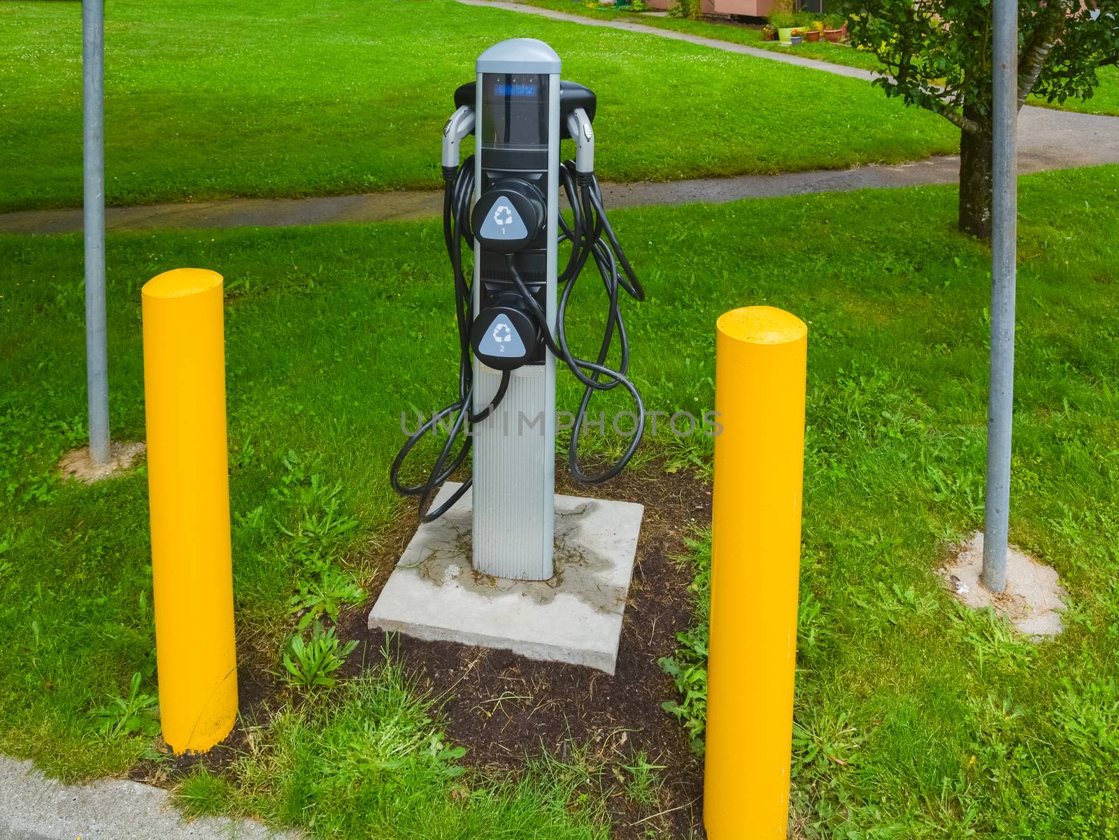 EV charger on green grass lawn. EV - electric vehicle charging station. Electric car charging point with yellow pillars around.