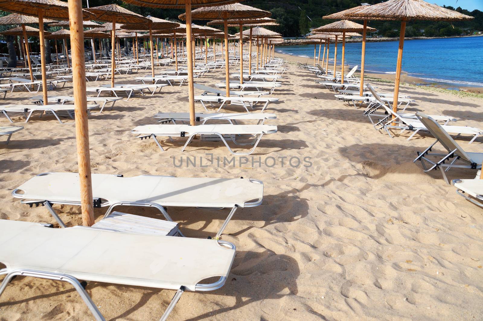 beach umbrellas and sun loungers on an empty beach by Annado