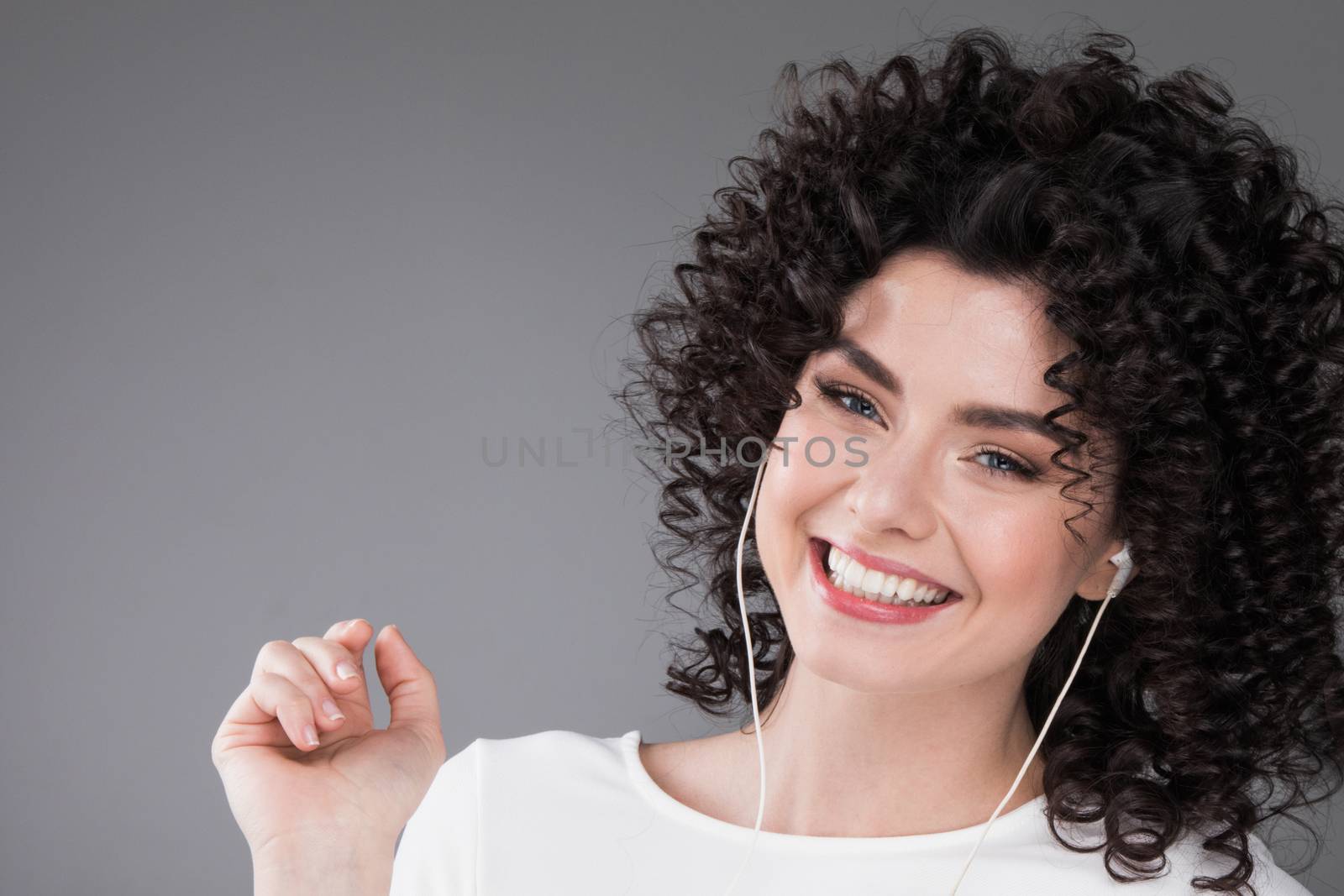 Woman in white dancing with earphones headphones listening to music, gray background