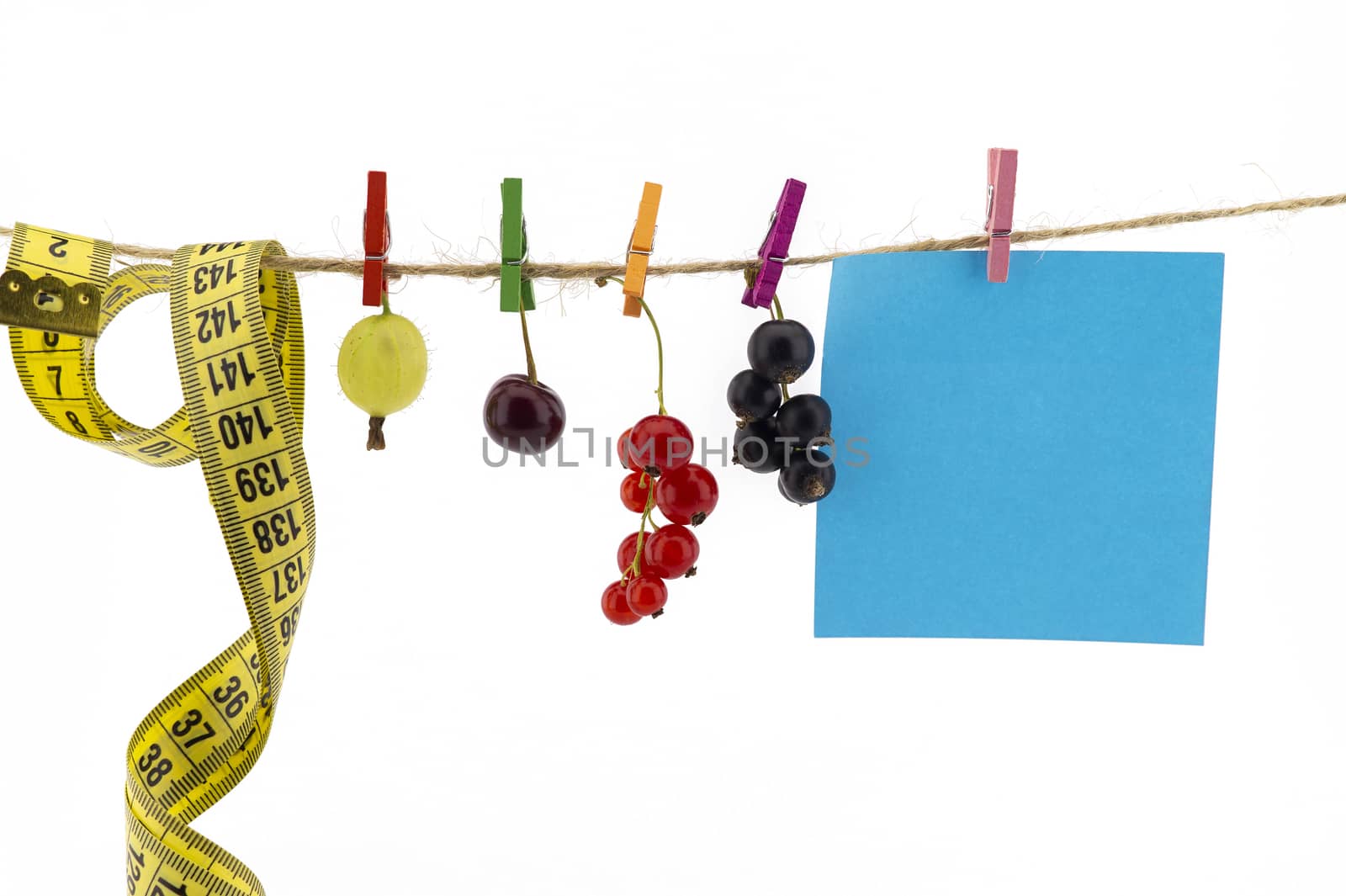 Fresh fruit, tape measure and blank sticky note hanging from clothes pegs on a rope with a gooseberry, red currants, cherry and black currants in a healthy diet concept