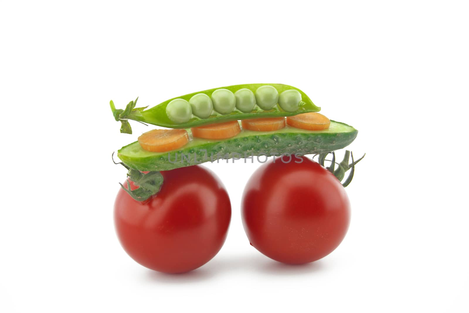 Healthy fresh vegetable still life over white with ripe red tomatoes, carrots, peas in a pod and cucumber balance on top of each other