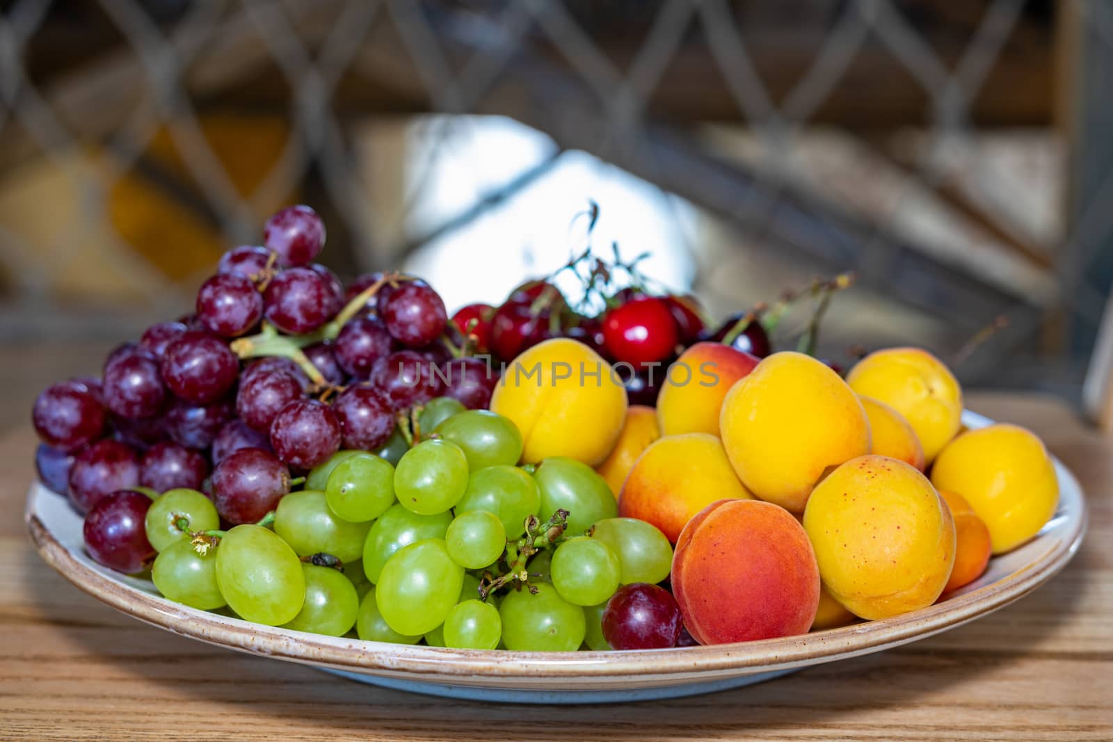 Fresh fruits on a plate. Fruit still life. Dish of fresh fruit. Grapes, cherries and peach on a plate. White utensils with fruits on a wooden surface