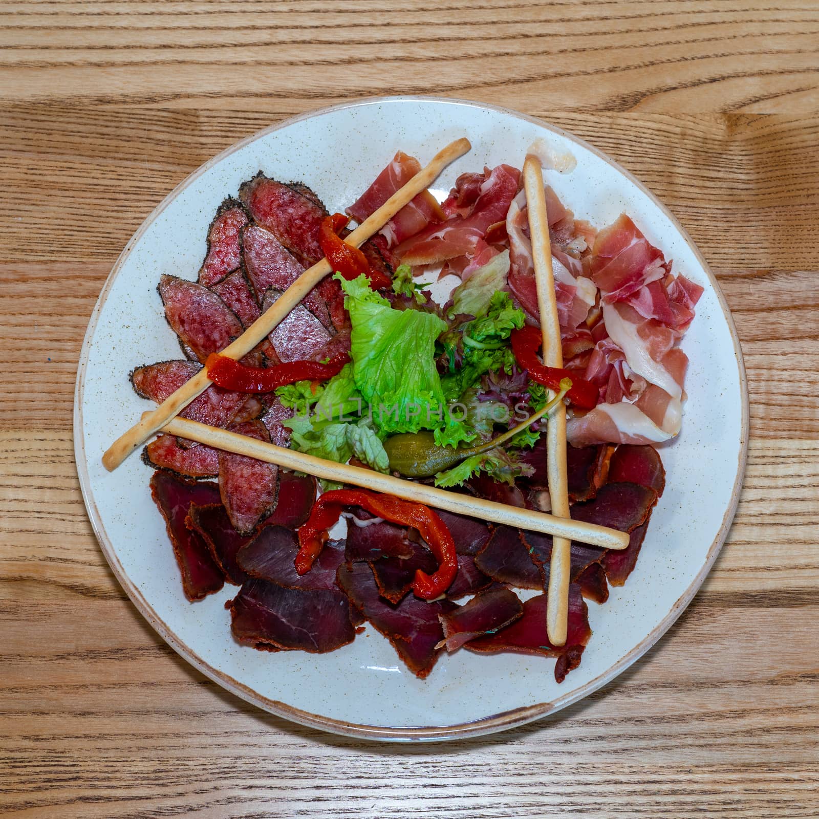 Plate with delicacies. Trio of dried delicacies. Basturma, prosciutto, sausage flat. White plate. Wooden table