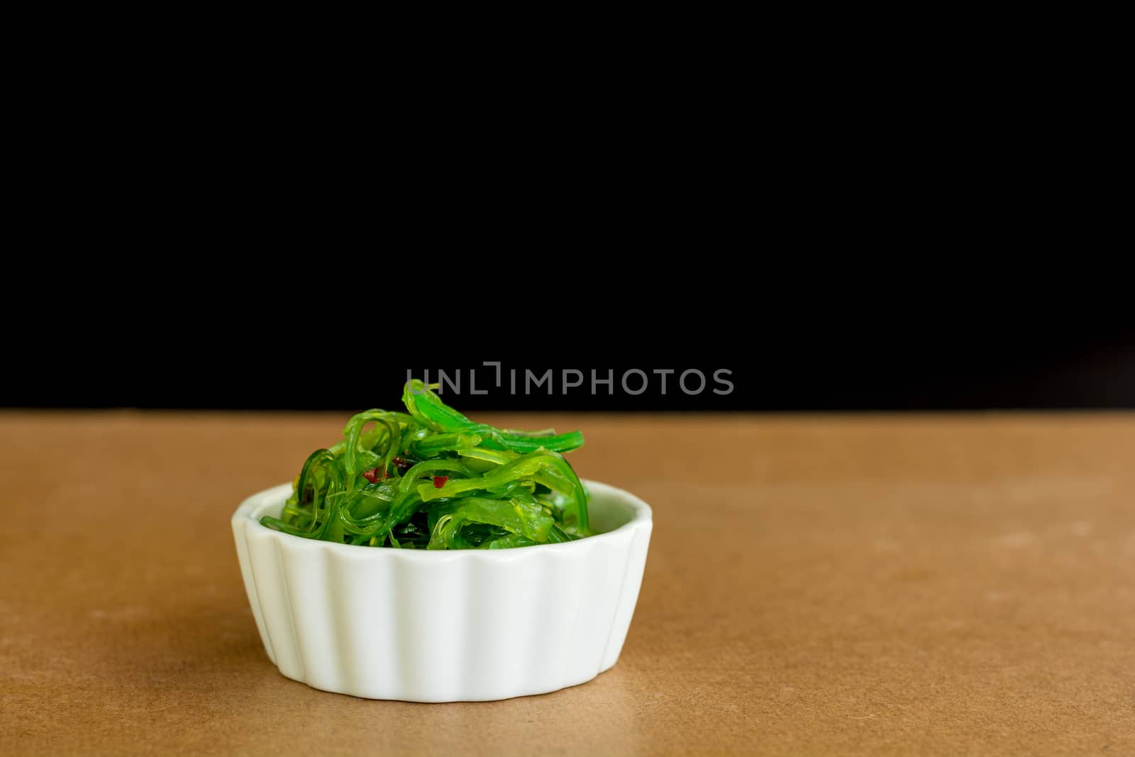 Japanese food concept. Fresh seaweed salad with sesame seeds in white bowl on black background.