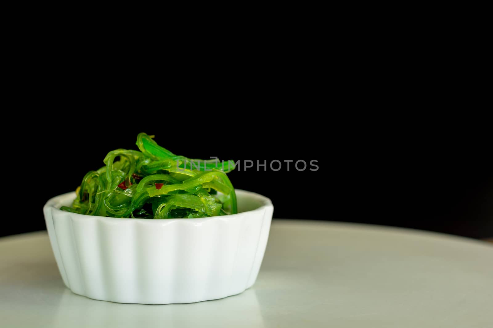 Japanese food concept. Fresh seaweed salad with sesame seeds in white bowl on black background.