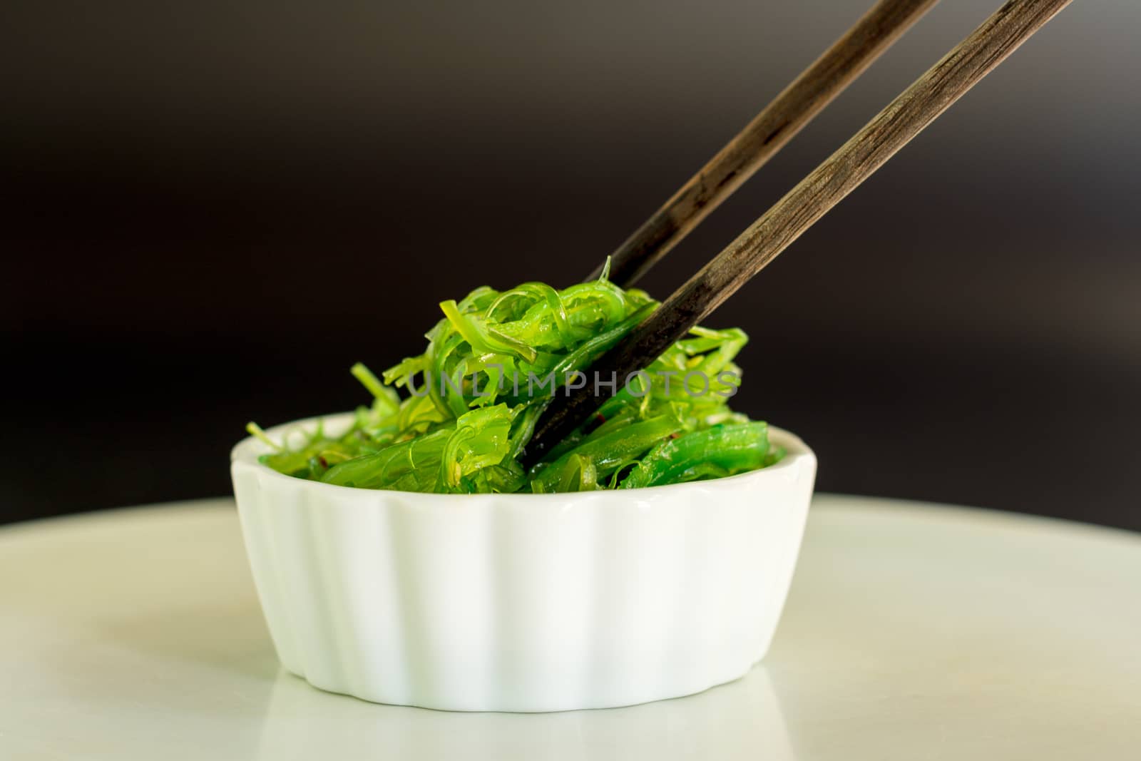 Japanese food concept. Fresh seaweed salad with sesame seeds in white bowl with chopstick on black background.