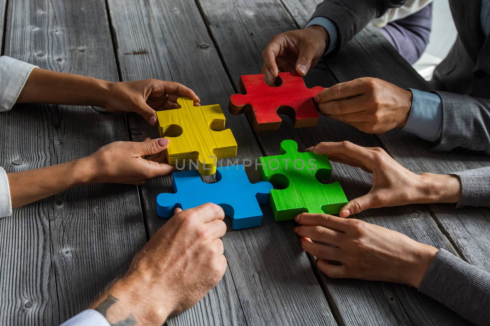 Business people team sitting around meeting table and assembling color jigsaw puzzle pieces unity cooperation ideas concept