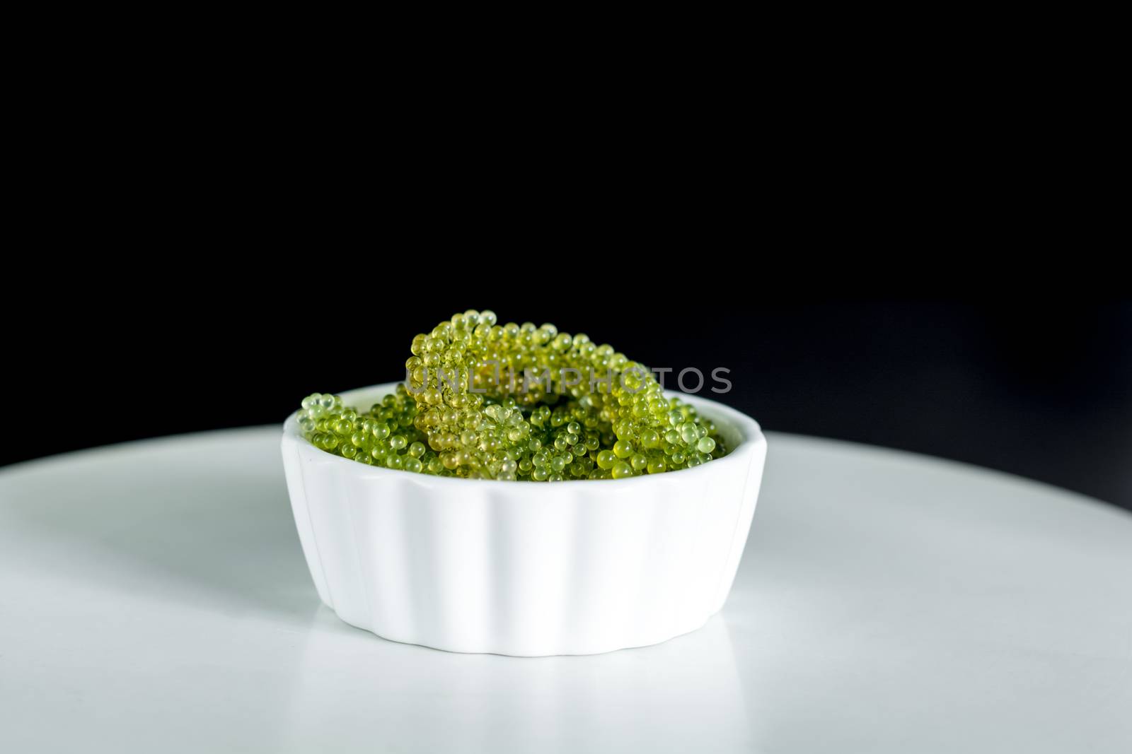 Fresh sea grapes or caviar seaweed in white bowl on black background. Healthy food concept.