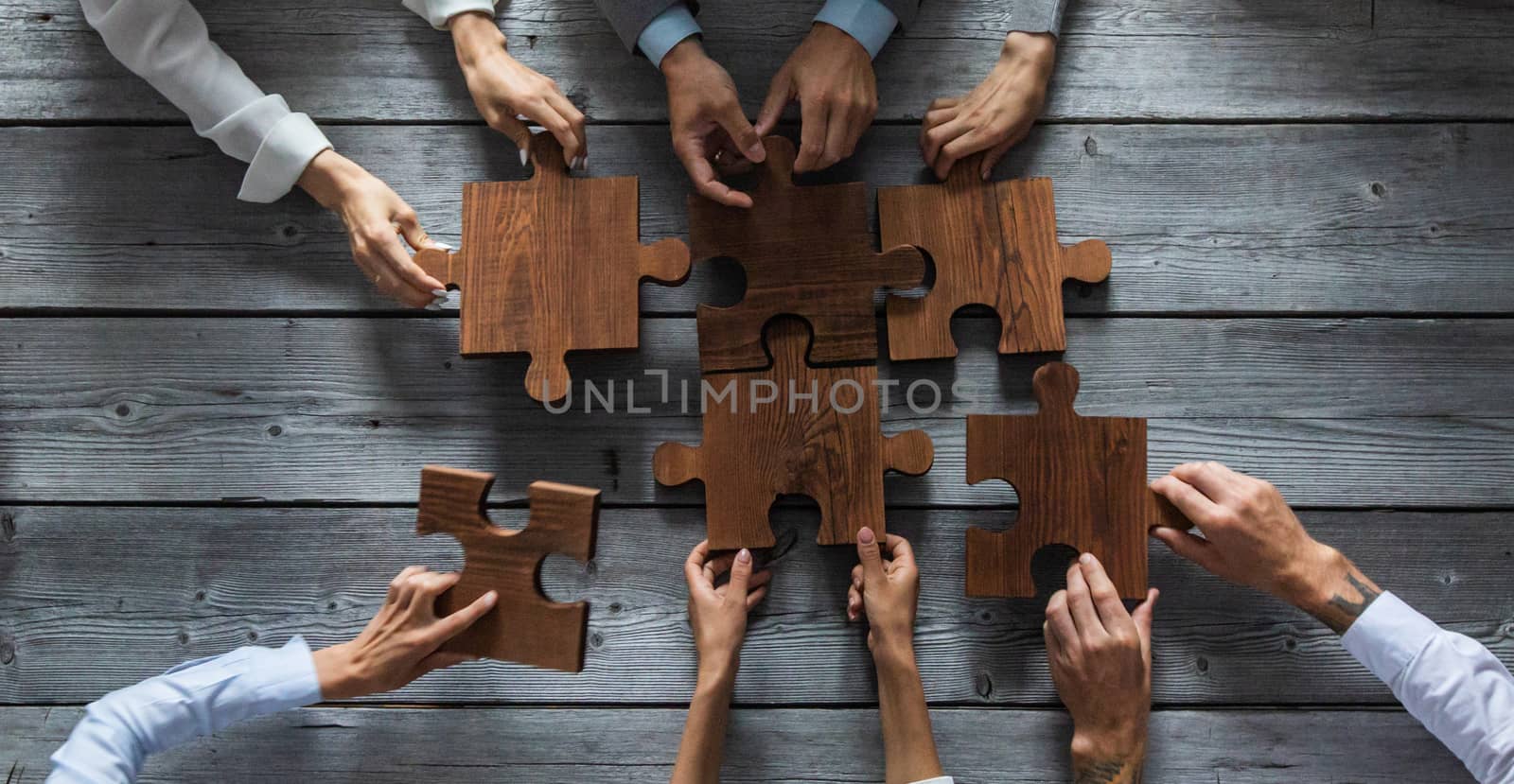 Business people team sitting around meeting table and assembling wooden jigsaw puzzle pieces unity cooperation ideas concept