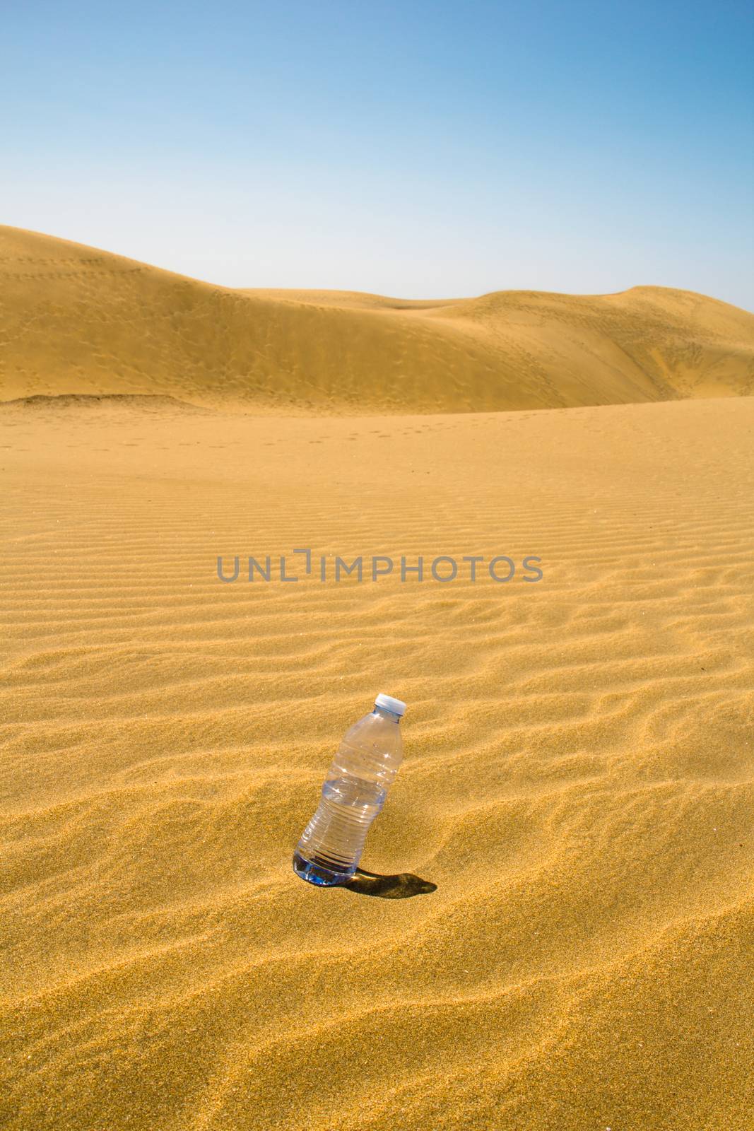 plastic bottle of water in the sand of the desert with blue sky